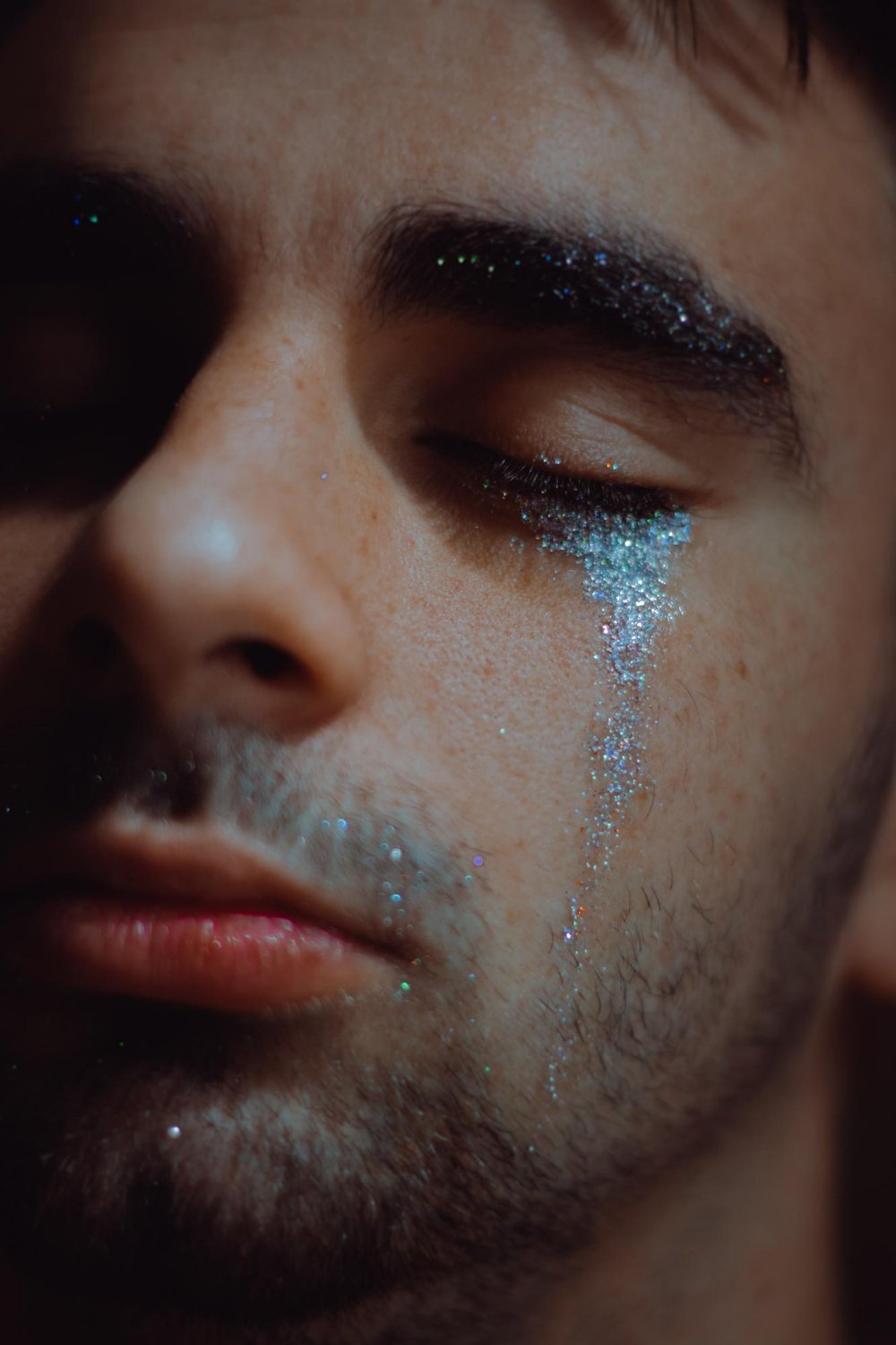 young man cries glittery tears with eyes closed