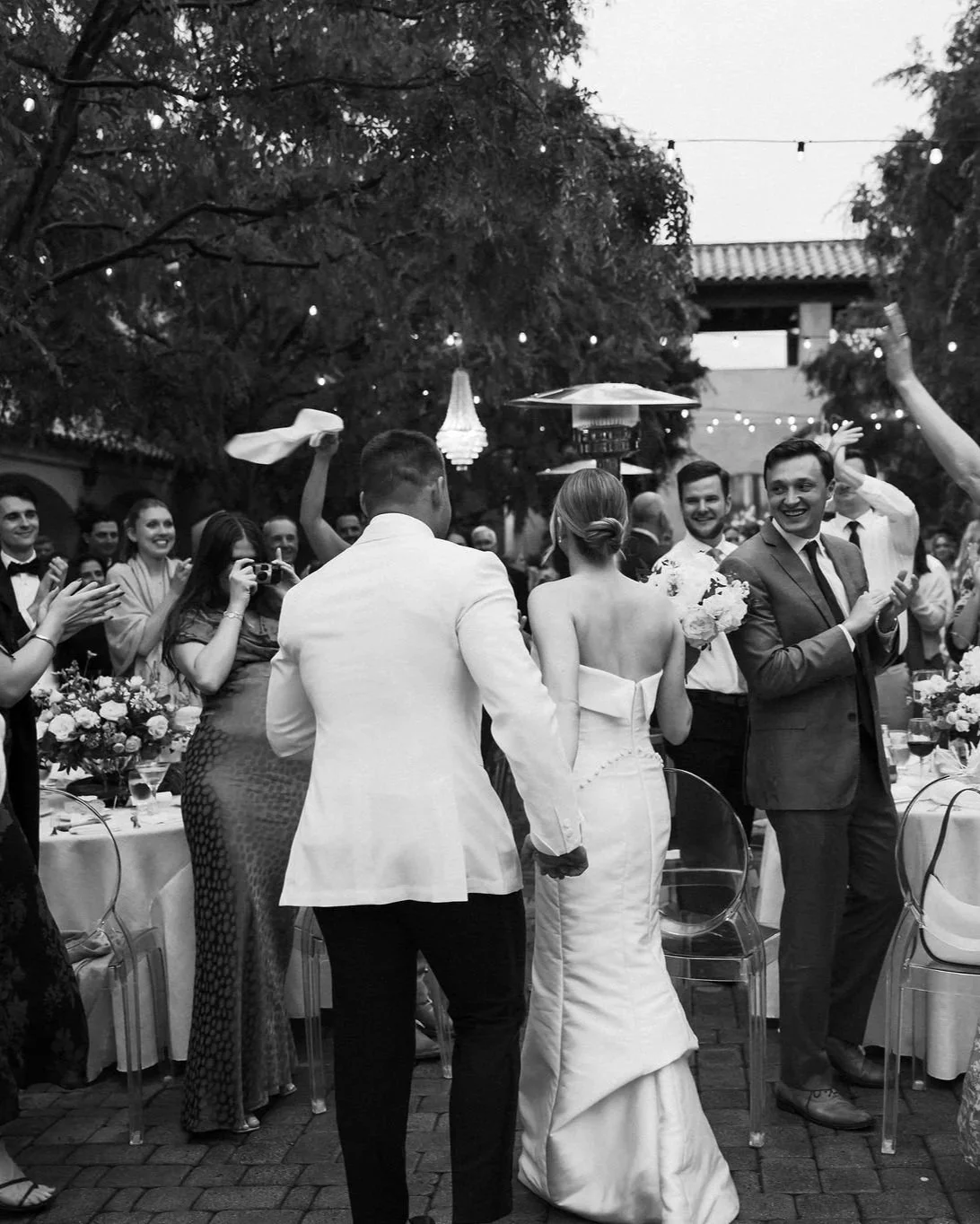 Bride and groom exiting ceremony with guests cheering in a black and white documentary wedding photo at Serra Plaza in San Juan Capistrano
