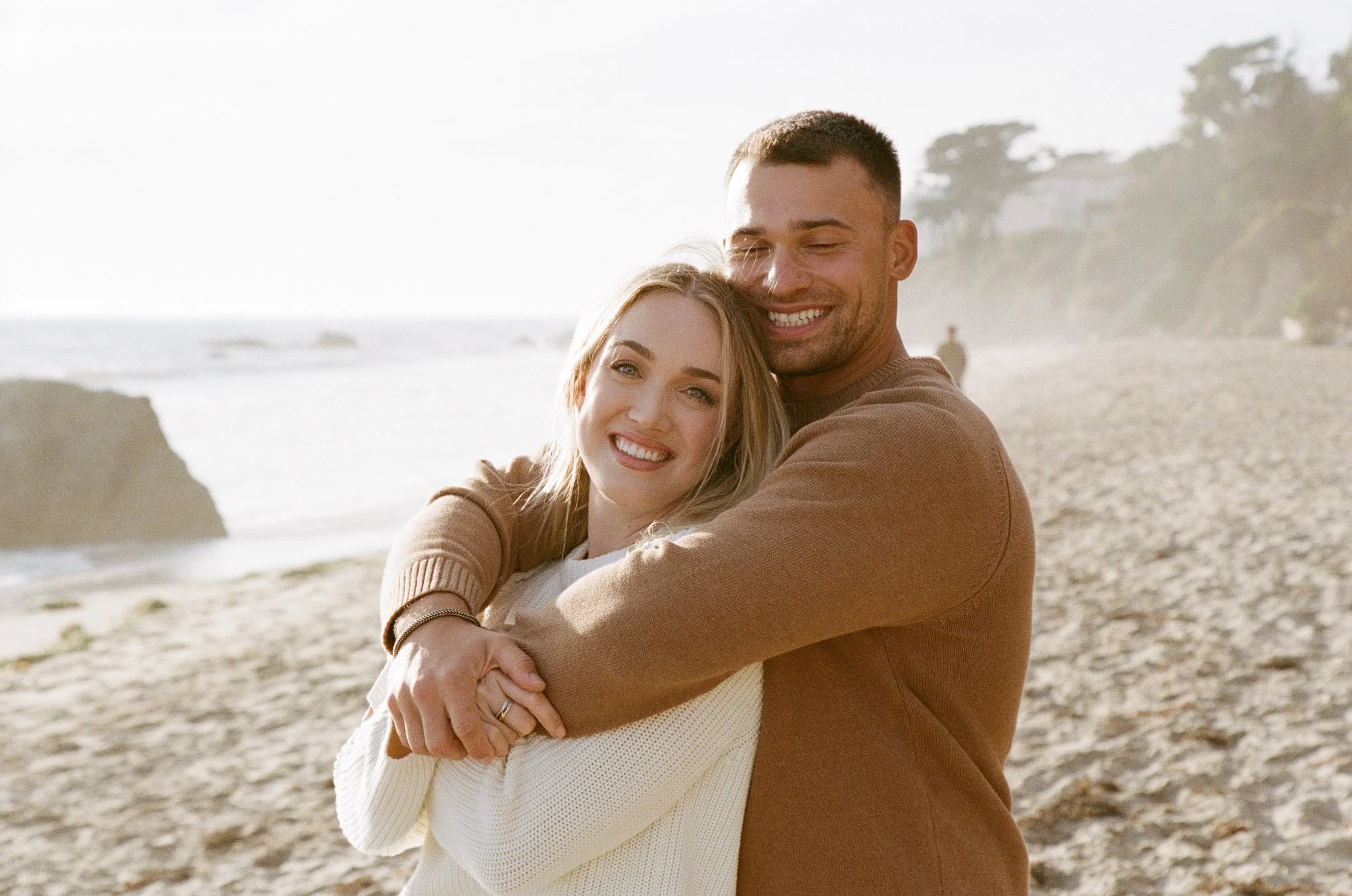 A smiling man and woman hugging on a beach during sunset.