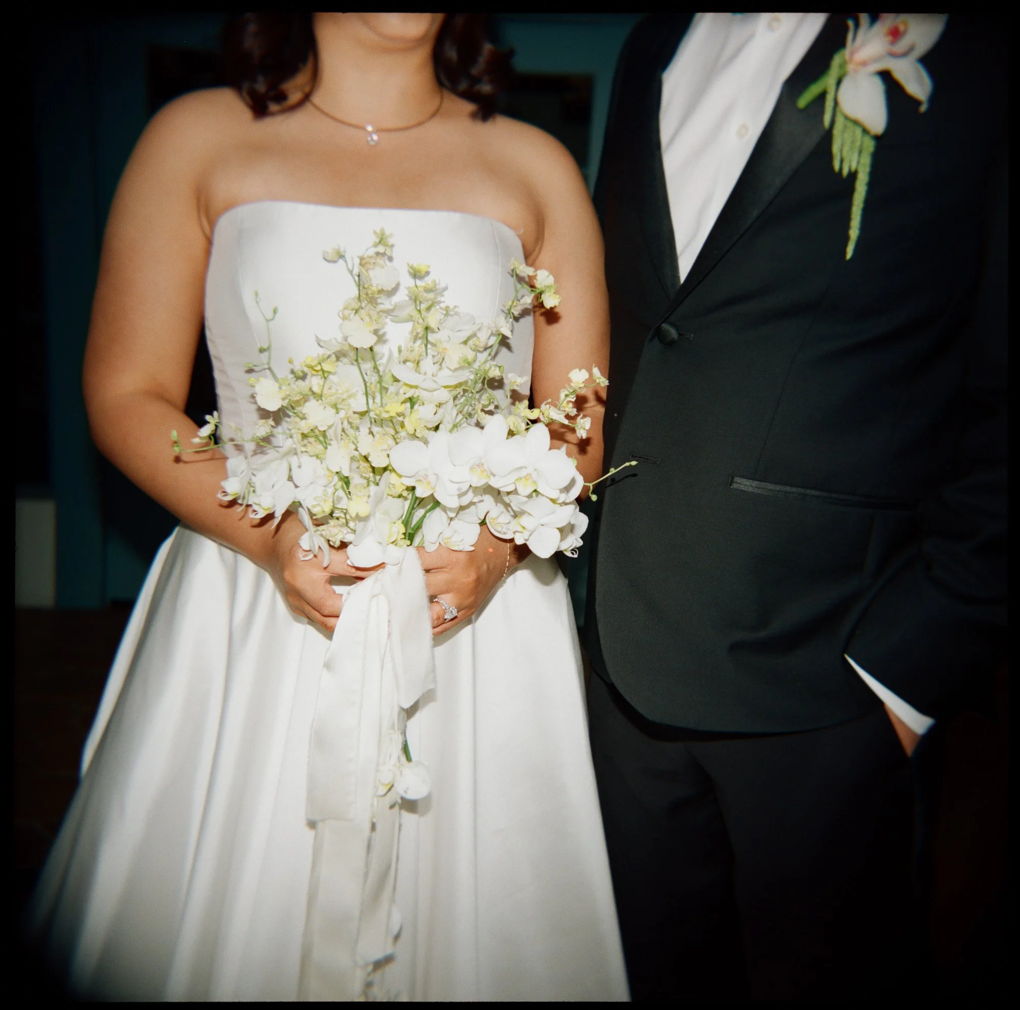 Close-up editorial wedding portrait of bride holding white cascading bouquet beside groom photographed on film