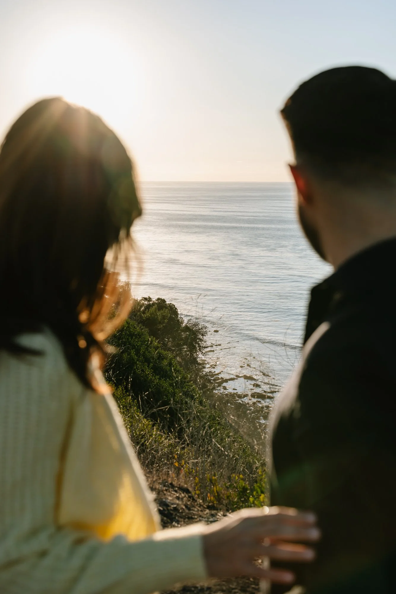 Two people sitting outdoors on a cliff overlooking the ocean during sunset.