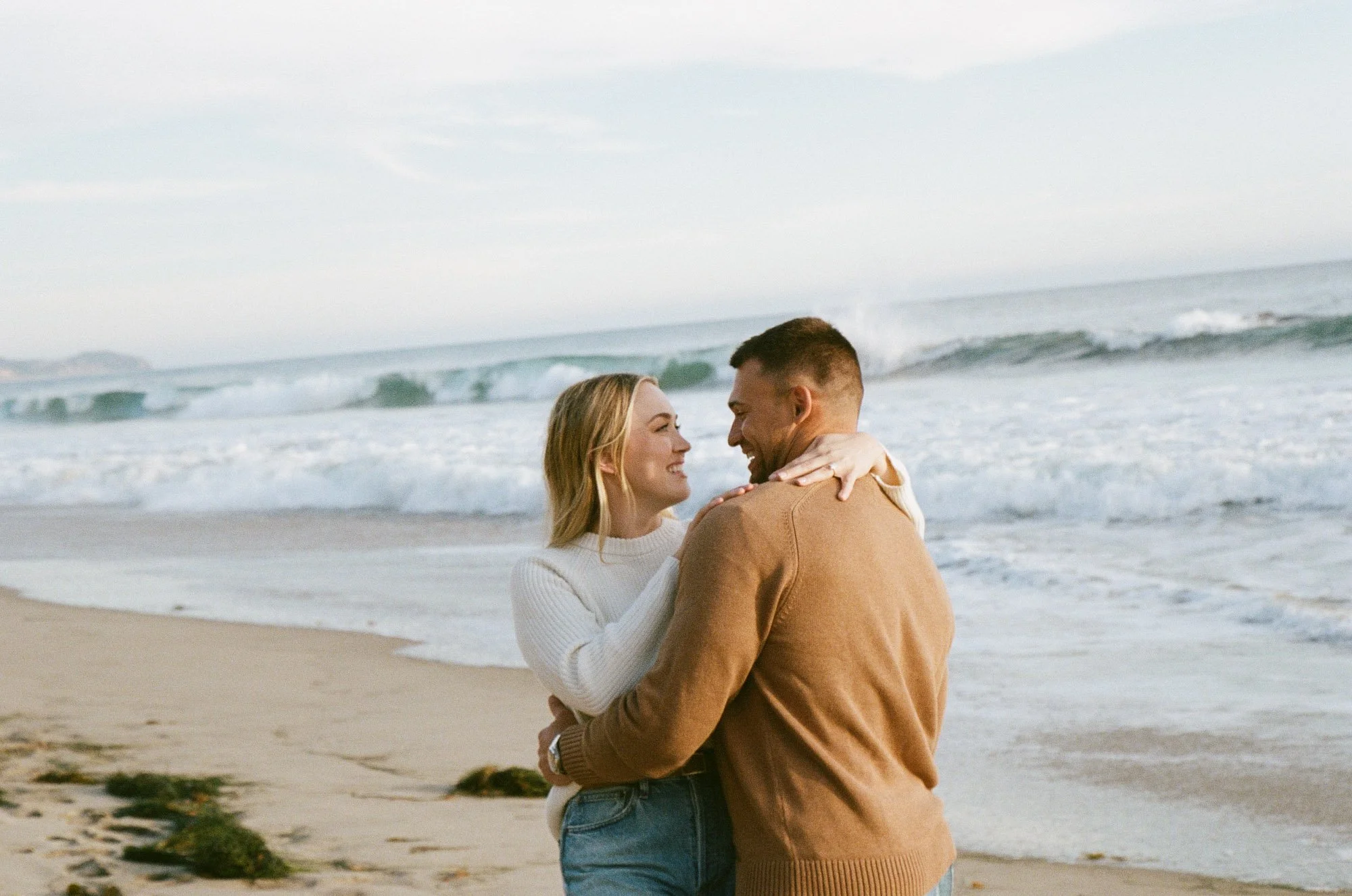A couple embracing on a beach with waves in the background