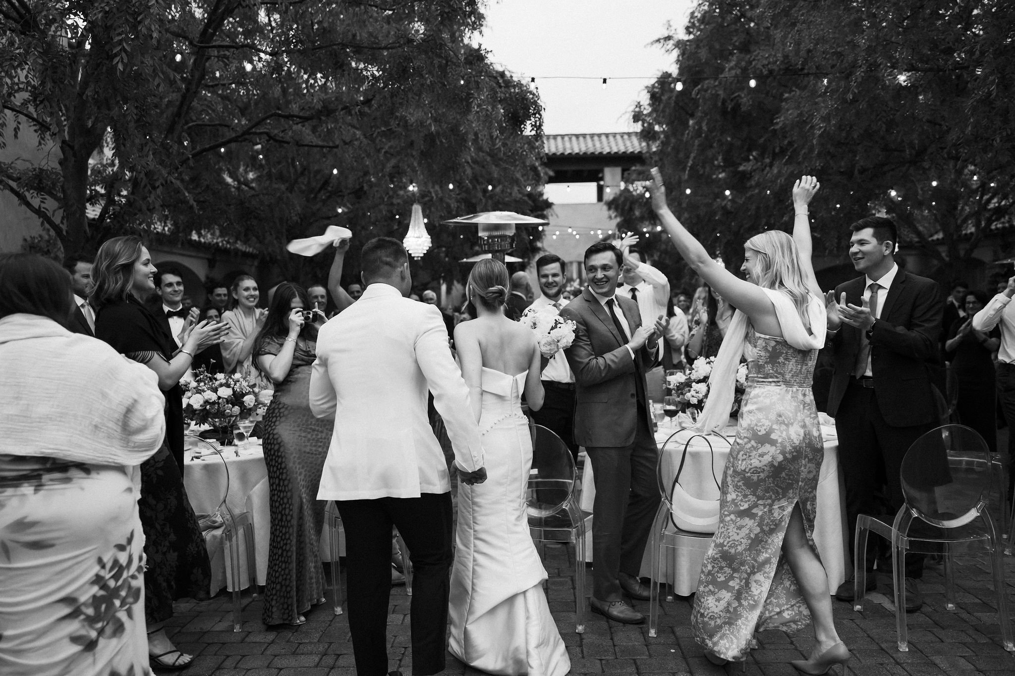 Bride and groom exiting ceremony with guests cheering in a black and white documentary wedding photo at Serra Plaza in San Juan Capistrano