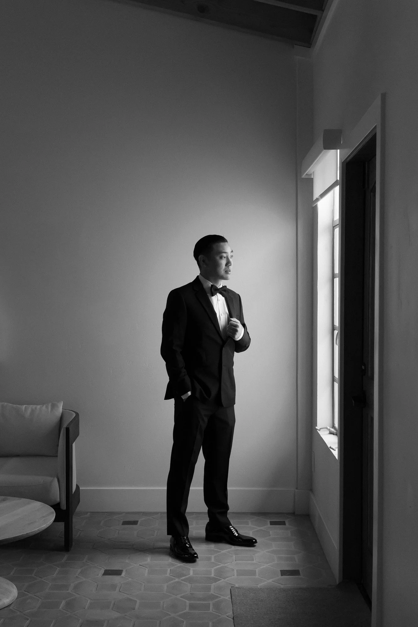 Black and white groom portrait in window light before a luxury California wedding