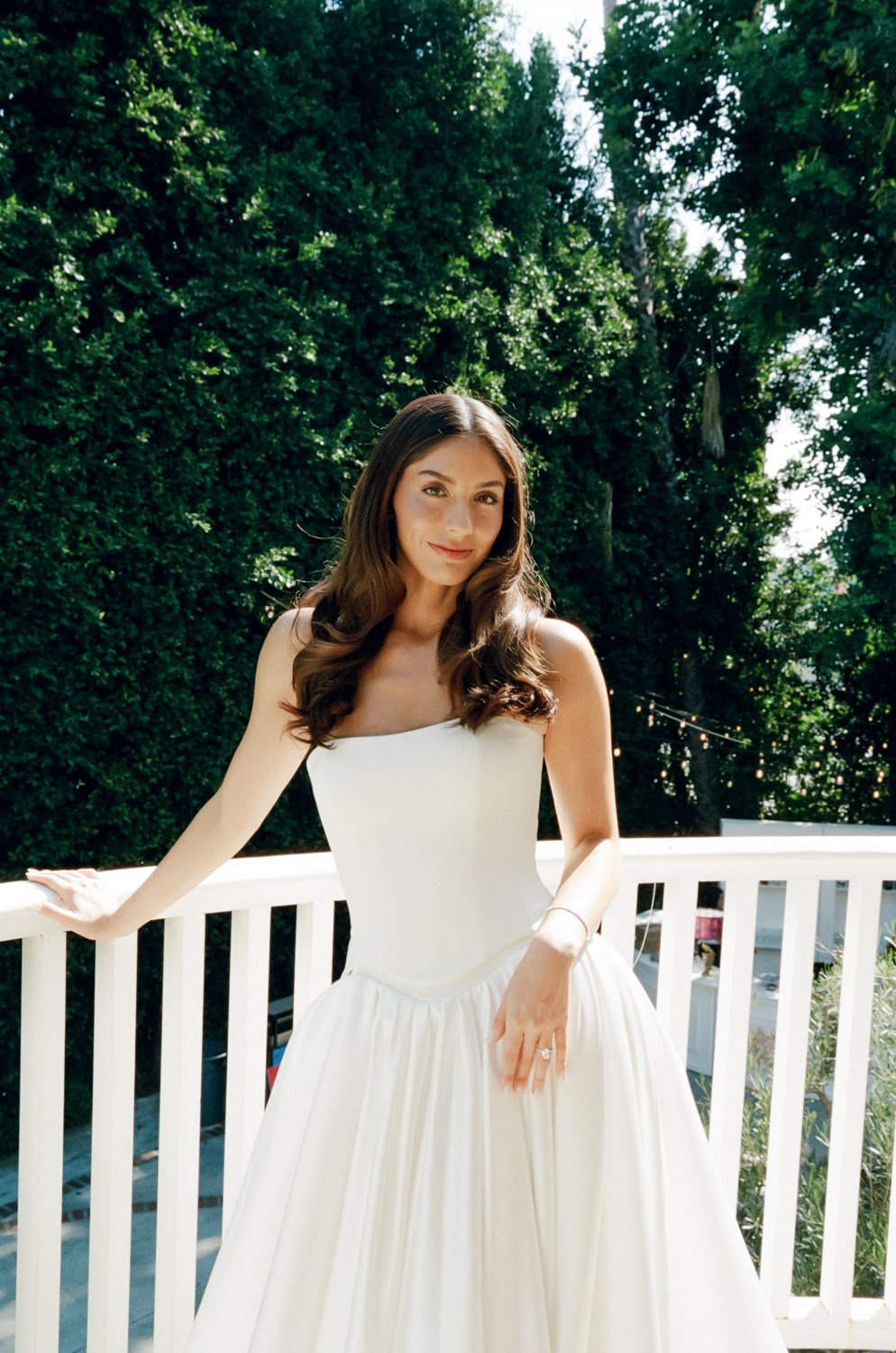 Bride in a white wedding dress standing outdoors on a patio with trees in the background. captured on film at a Los Angeles luxury wedding