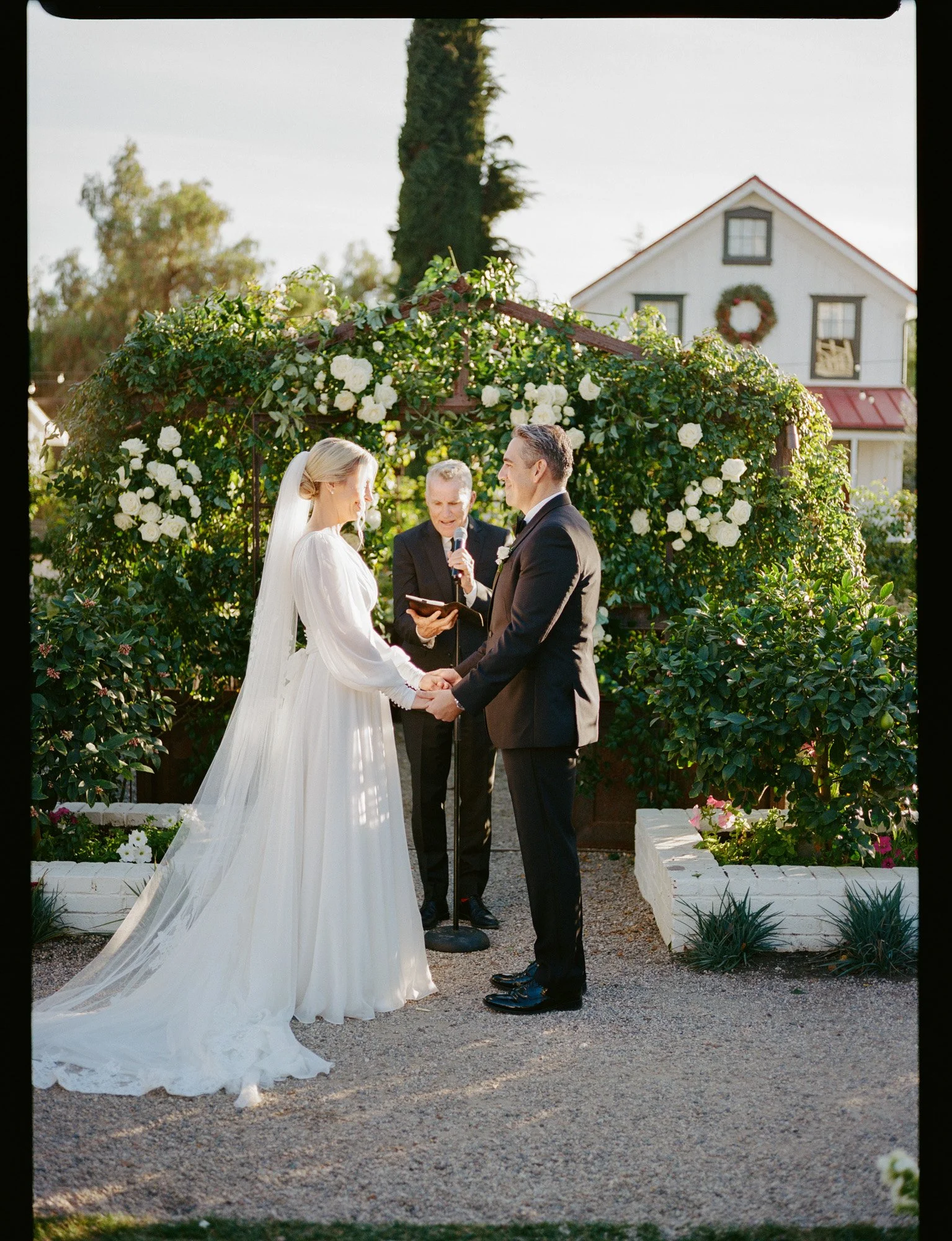 Outdoor wedding ceremony with bride and groom set against the iconic greenhouse at the Inn at Mattei's Tavern in Los Olivos, California. captured on film photography