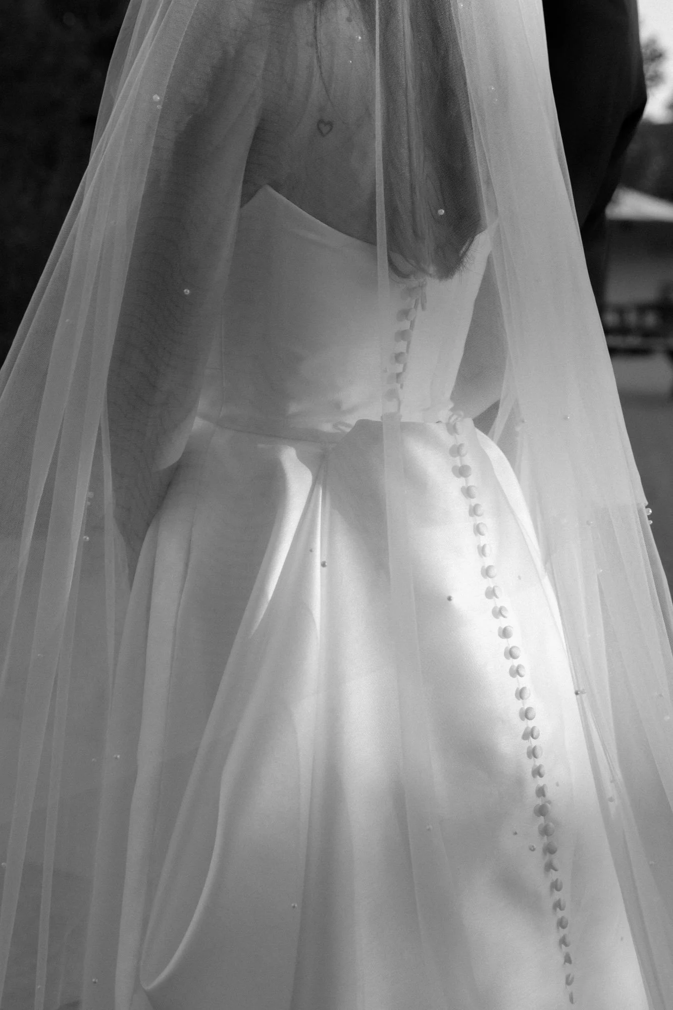 Black and white close-up of bridal veil and wedding dress covered buttons photographed in an editorial style