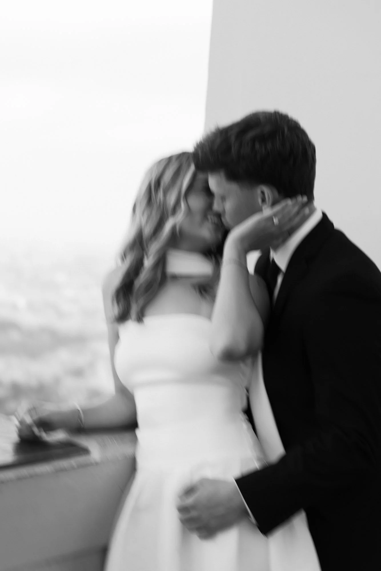 A black-and-white photo of a bride and groom close together at their wedding, holding hands, with the bride gently touching the groom's face.
