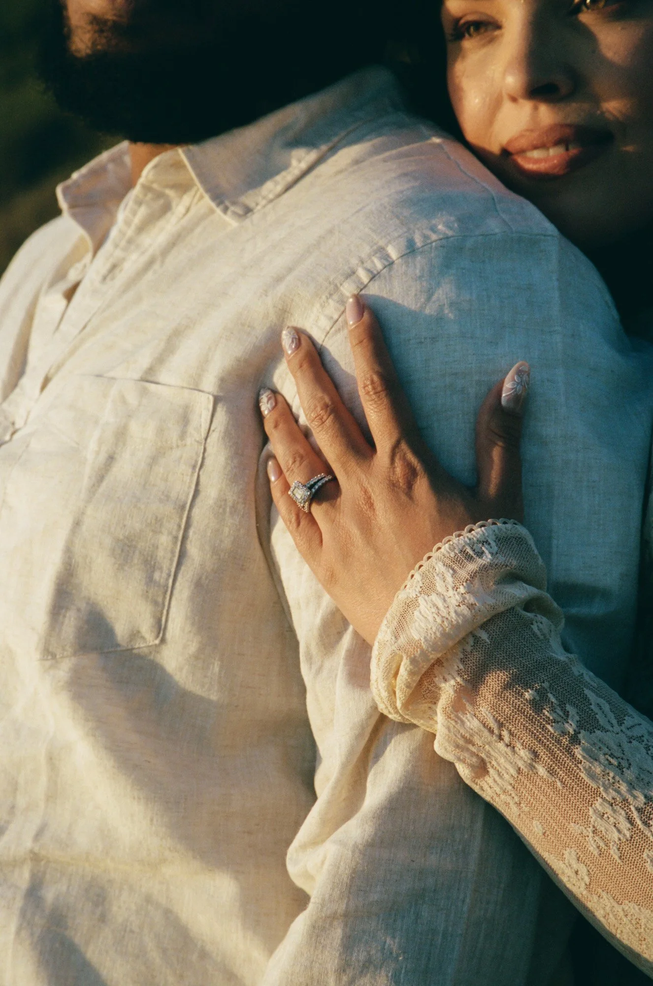 A woman with earrings and rings holding onto a person wearing a cream-colored shirt with lace details on the sleeves.