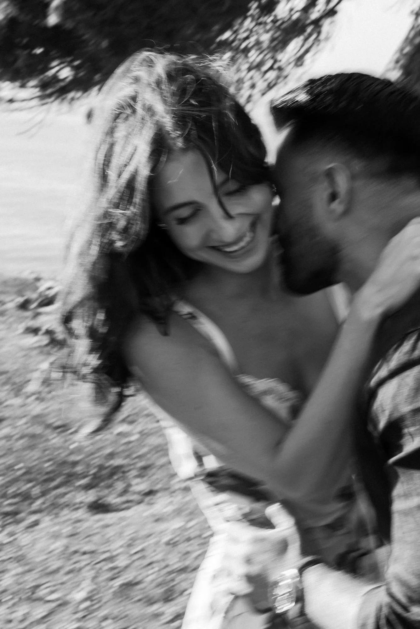 A black and white photo of a smiling woman with long hair and a man close to her, outdoors, possibly on a hike or walk, with trees and grass in the background.
