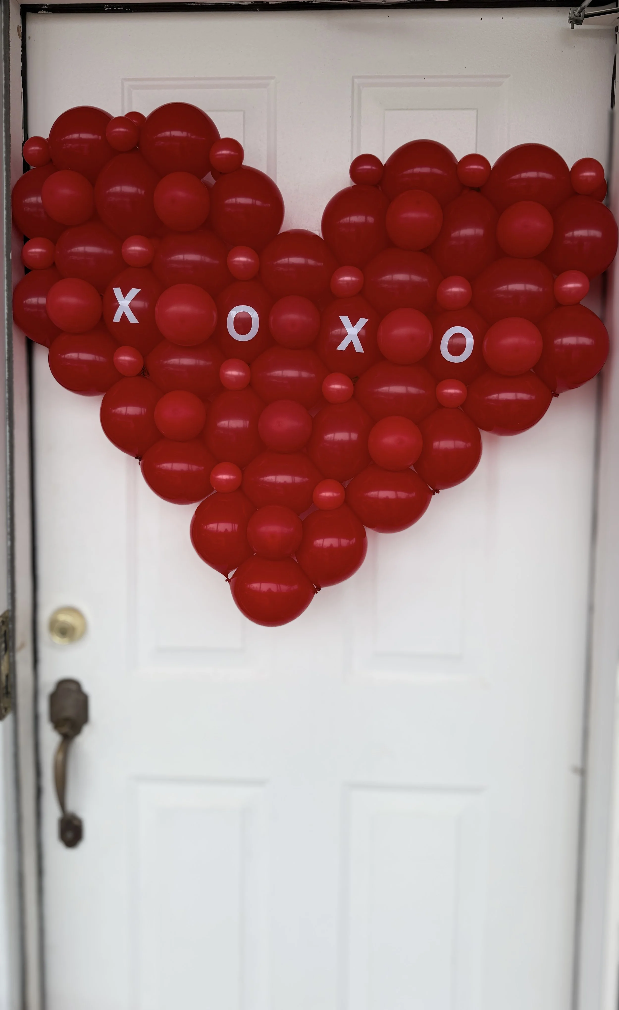 Red heart-shaped balloon decoration on a white door with the words 'XOXO' spelled out in white letters.