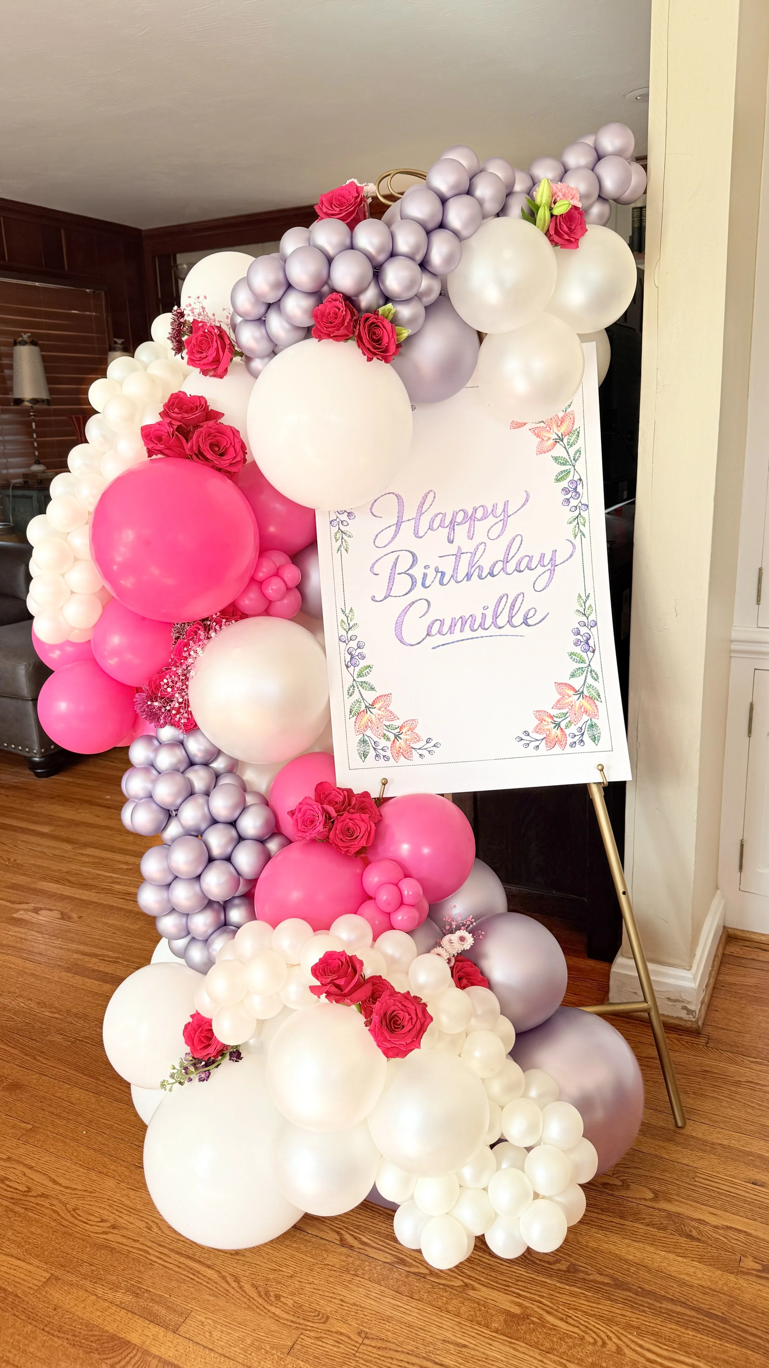 Balloon arch with pink, white, and lavender balloons, decorated with pink roses and a birthday sign reading 'Happy Birthday Camille' in floral letters.