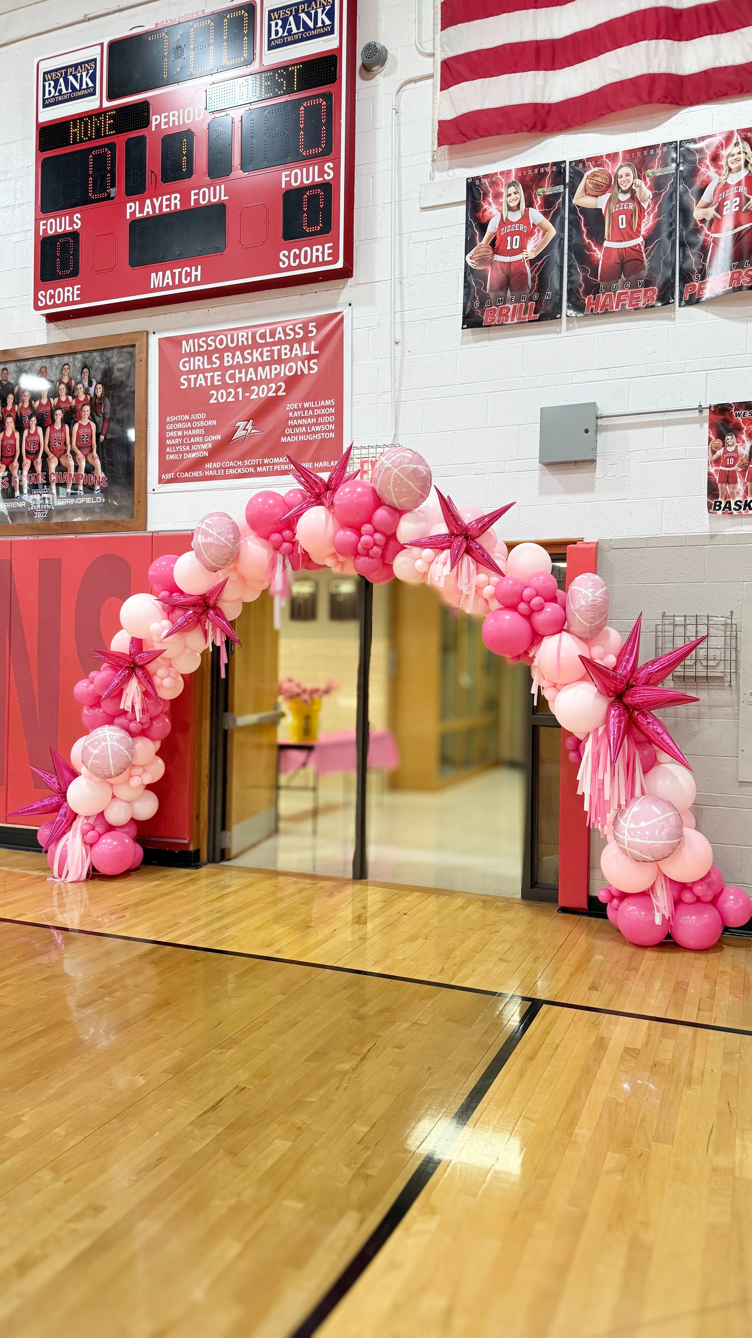 Basketball gym entrance decorated with pink and white balloons and star-shaped balloons for a celebration or event.