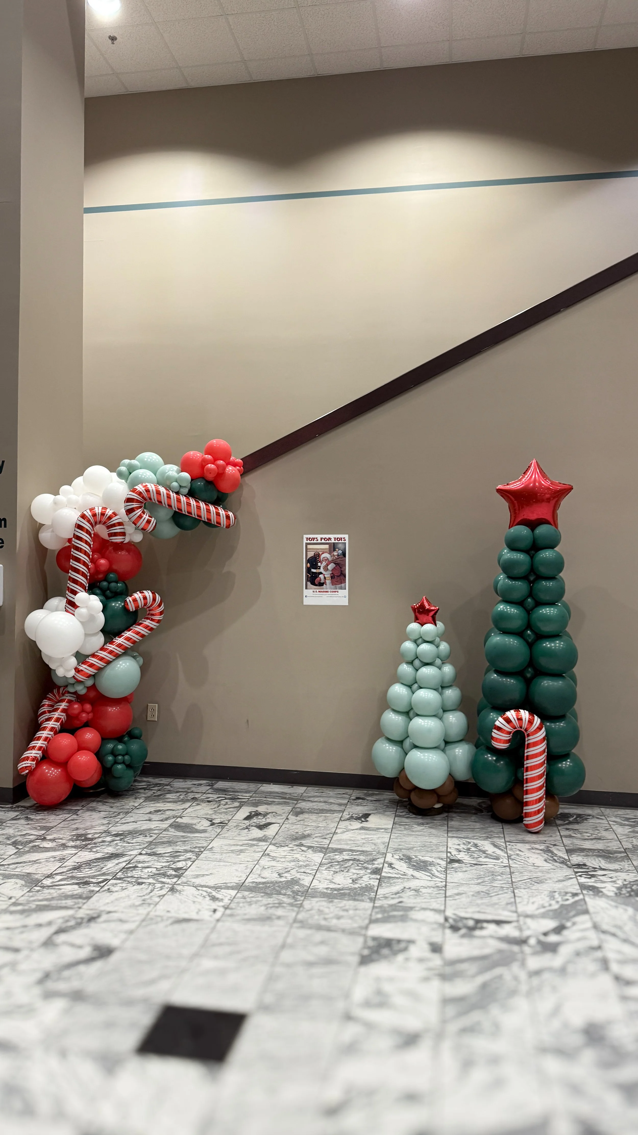 Holiday balloon tree decorations with red, white, and green balloons and candy cane accents inside a building.