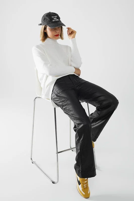 Person in black cap, white sweater, black pants, yellow sneakers sitting on a white chair against a plain background.