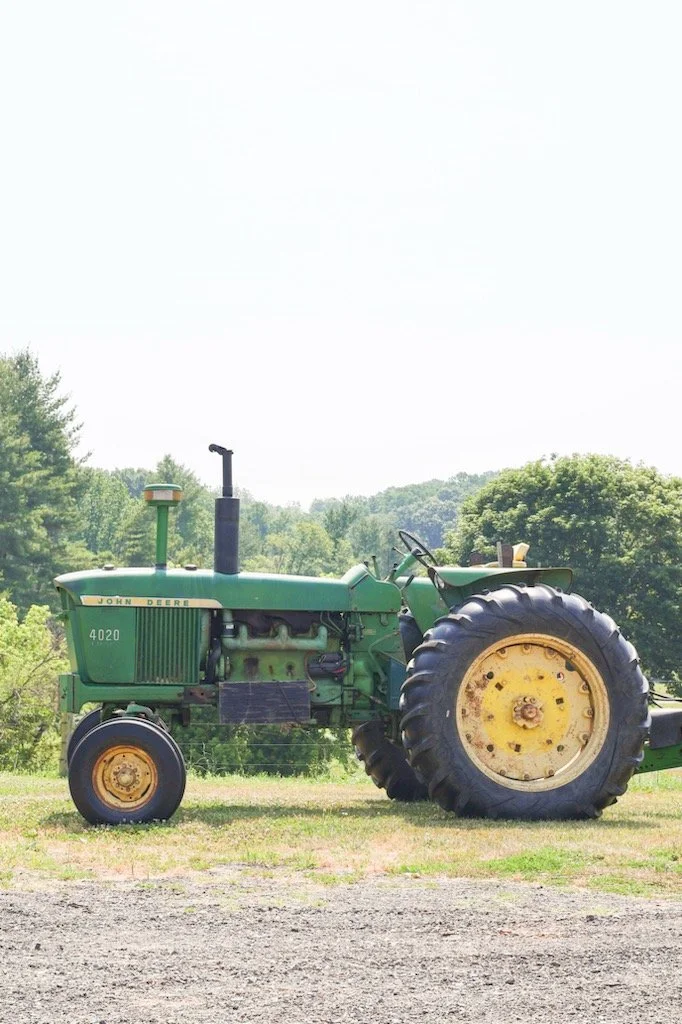 Green John Deere tractor with yellow wheels parked on grass with trees in the background.