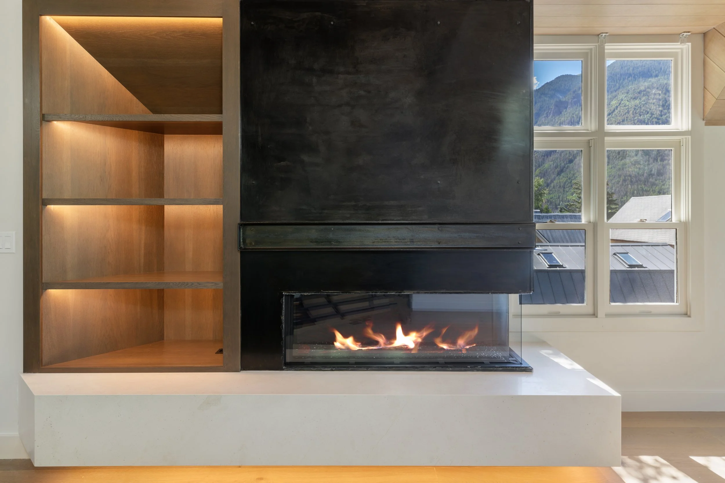 Custom-lit walnut shelving and three-sided linear gas fireplace with blackened steel surround, Telluride, Colorado home.
