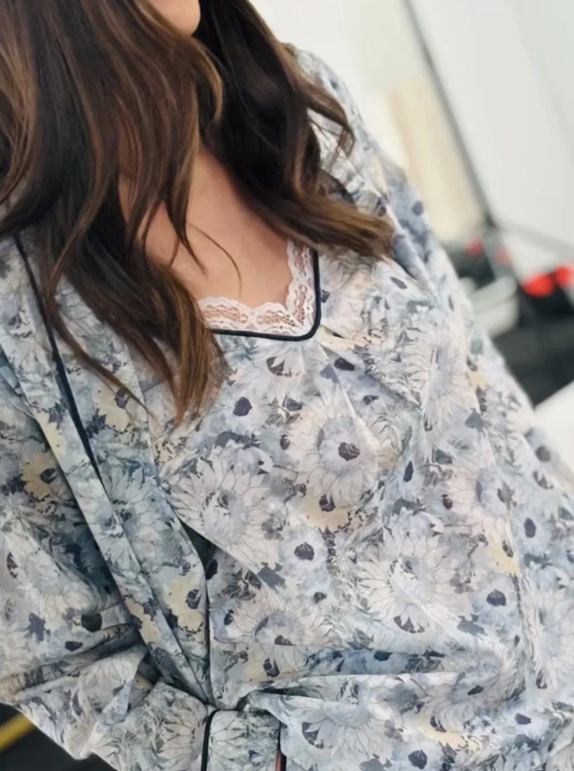 Close-up of a woman wearing floral pajamas with lace trim underneath, showing her chest and part of her brown hair.