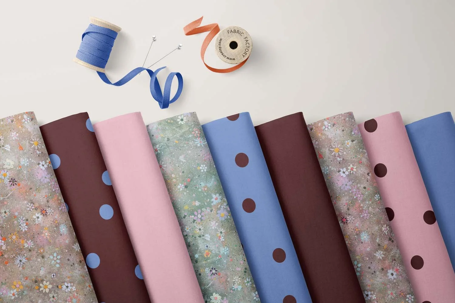 Multiple rolls of fabric with various floral, polka dot, and solid patterns, along with sewing pins and thread on a white background.