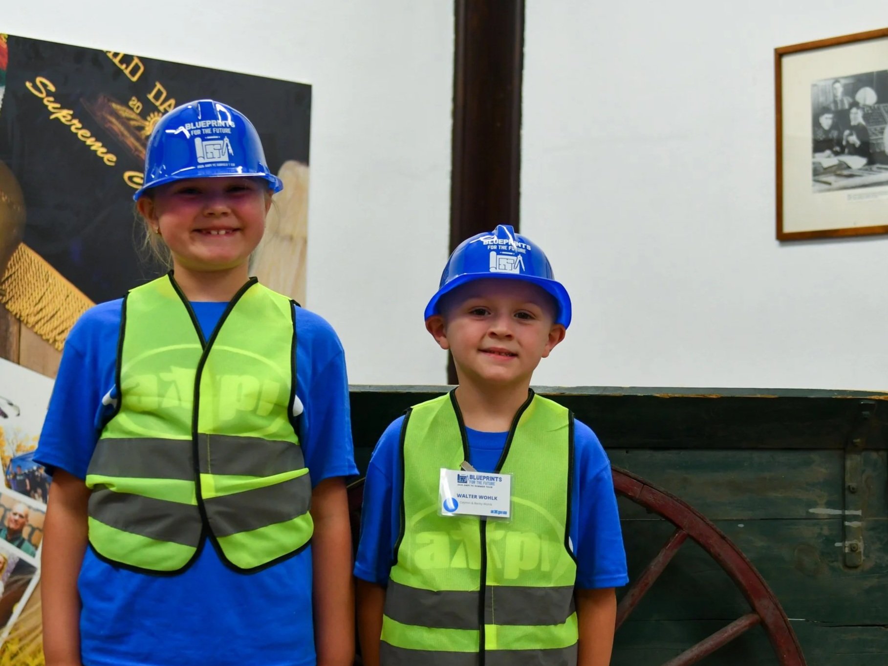   Cora and Walter Wohlk, children of Clayton and Becky Wohlk of Almena, Wis., showcase their new event- themed hard hat and construction vest provided for members during the summer tour.  