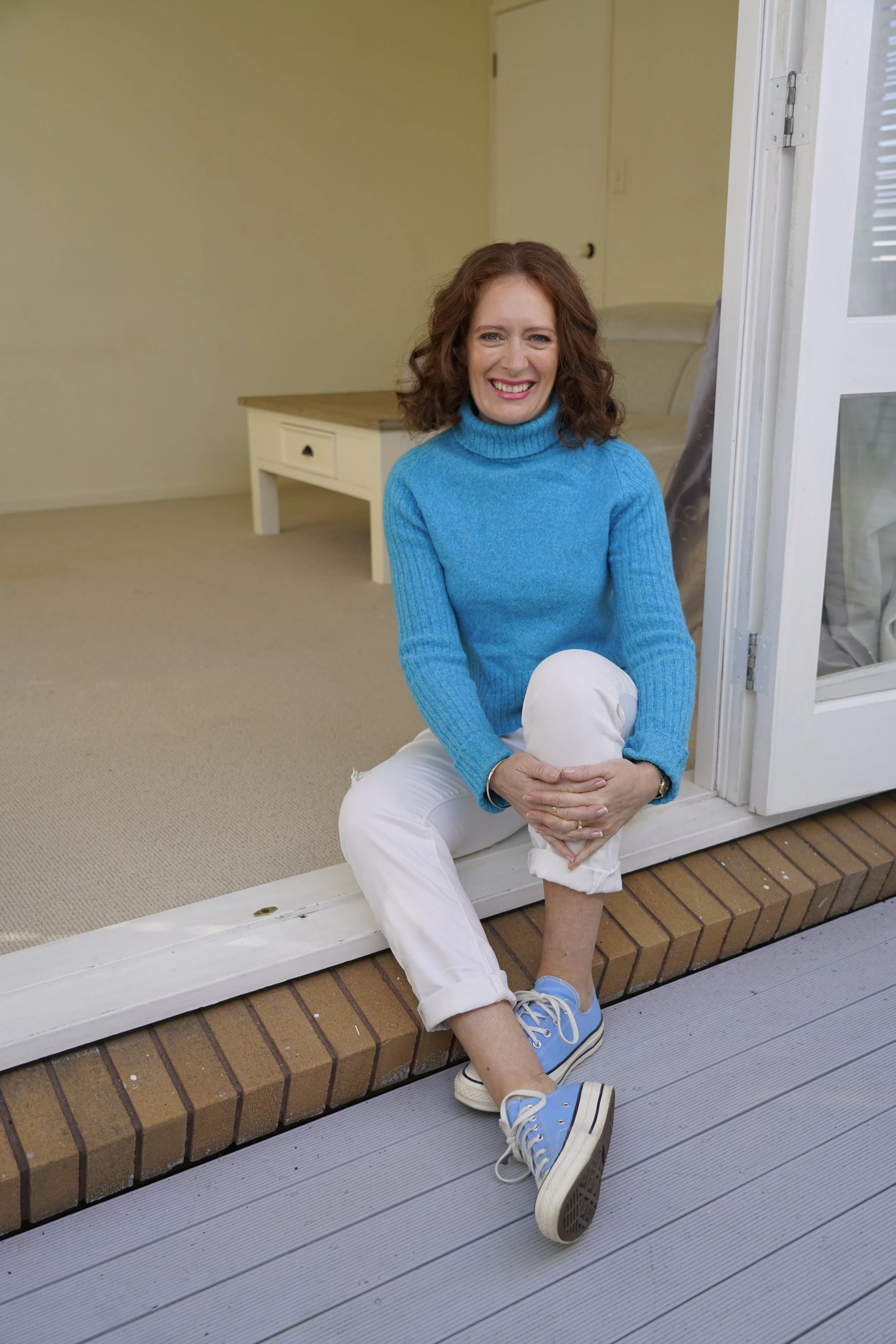 Carmel smiling sitting in doorway in blue sweater