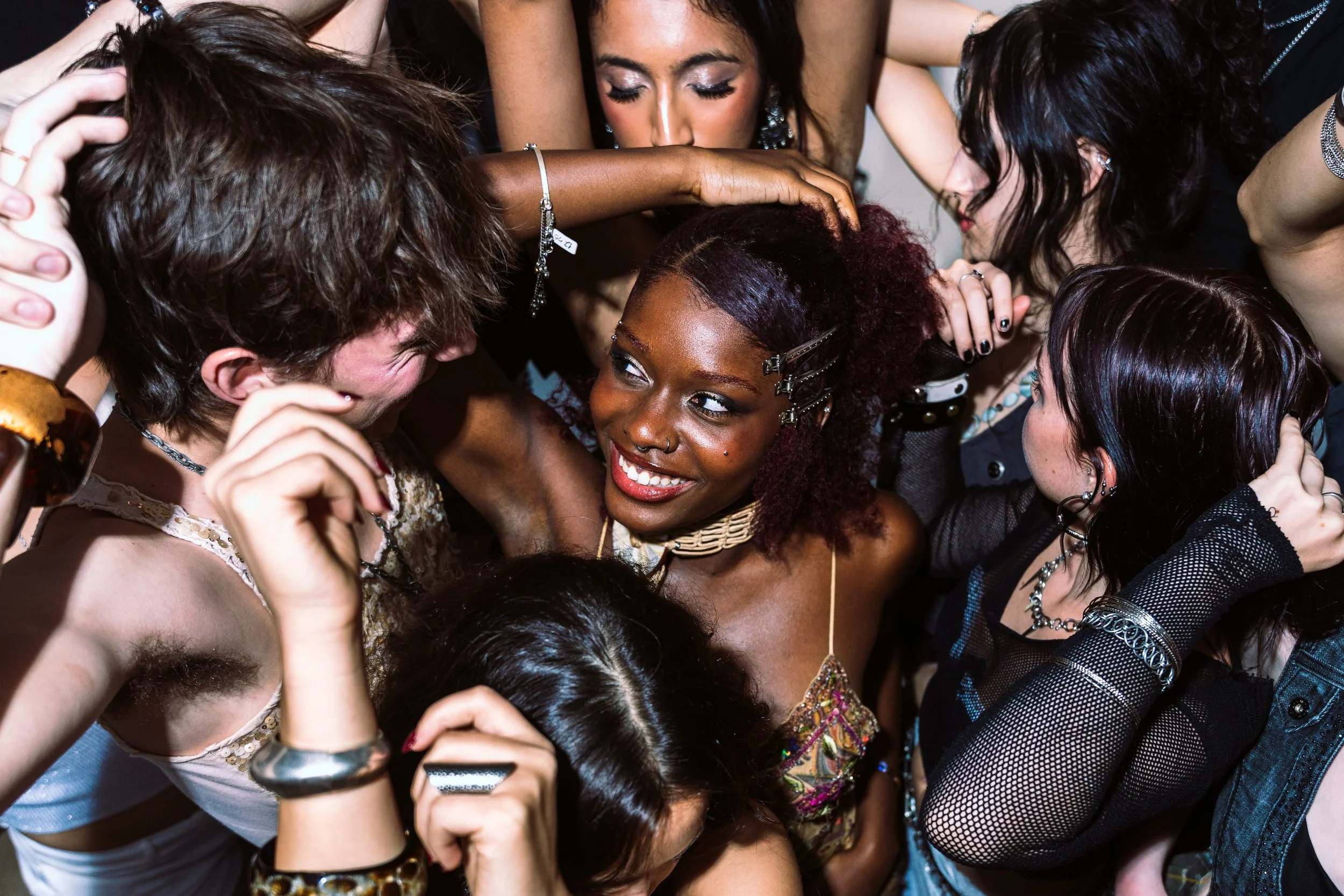 Group of diverse young women crowded closely together, laughing, smiling, and embracing each other at a party or celebration.