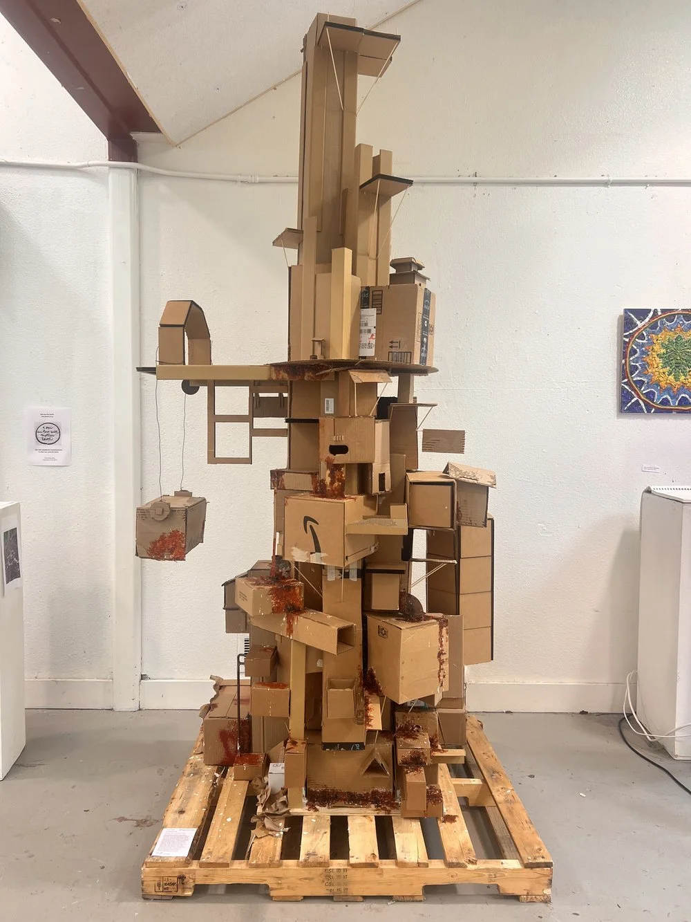 Sculpture made of stacked and arranged cardboard boxes on a wooden pallet in an art gallery.