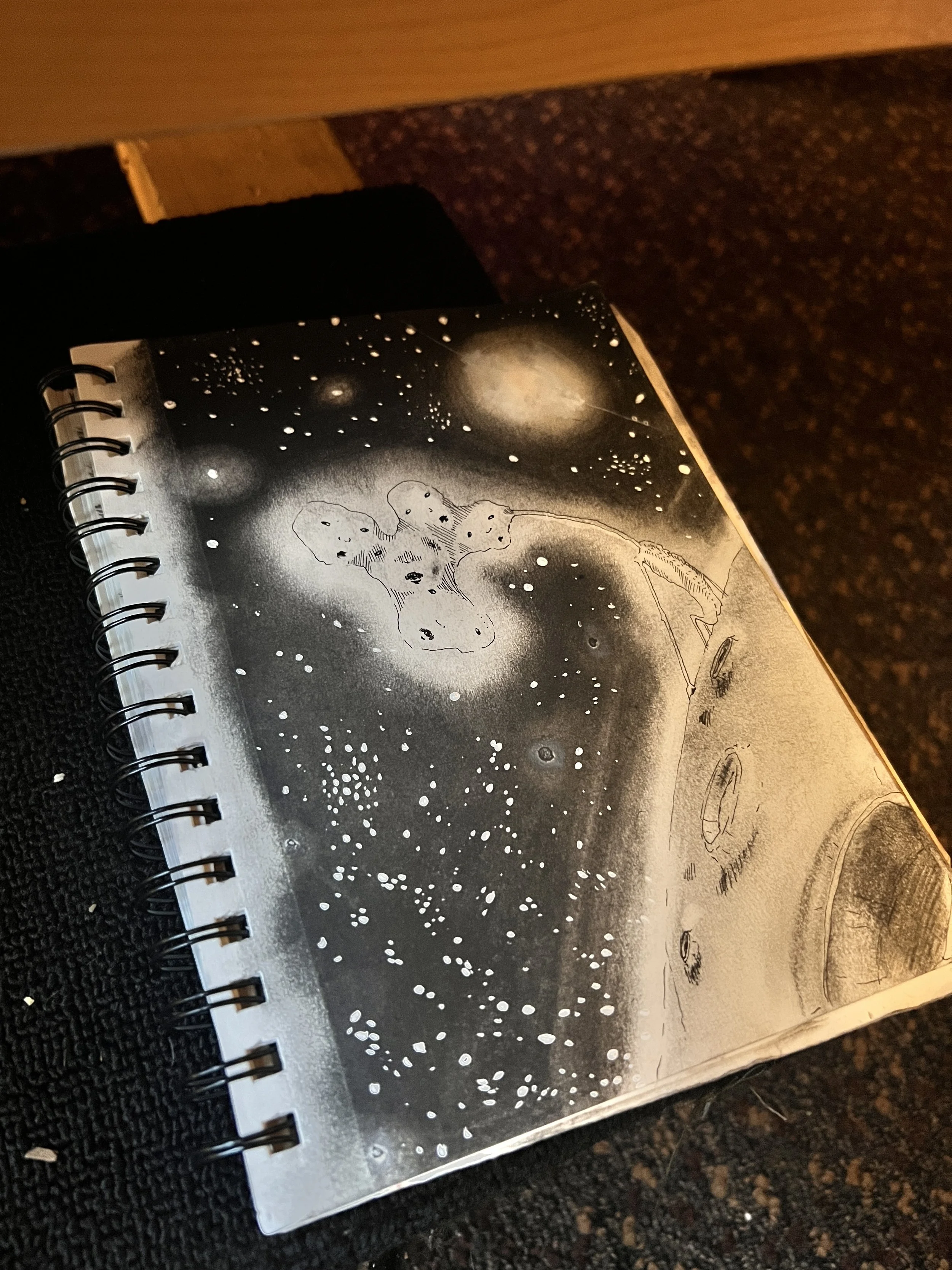 A black and white space-themed drawing featuring stars, planets, and a spaceship in outer space.
