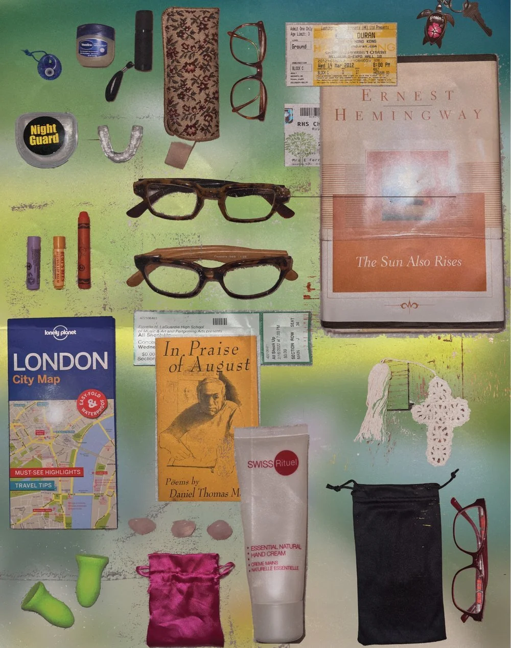 A flat lay of various personal items including glasses, a book titled "Ernest Hemingway - The Sun Also Rises," a travel ticket to Hong Kong, a small London city map, a book titled "In Praise of August" by Daniel Thomas M, a tube of Swiss Rituel hand 