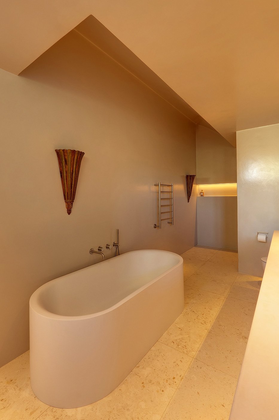 Modern bathroom with a freestanding bathtub, wall-mounted faucets, two wall sconces, a towel rack, and a recessed shelf with lighting