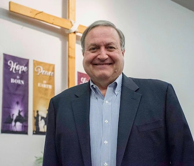 Smiling man with blue shirt and gray suit jacket in church.