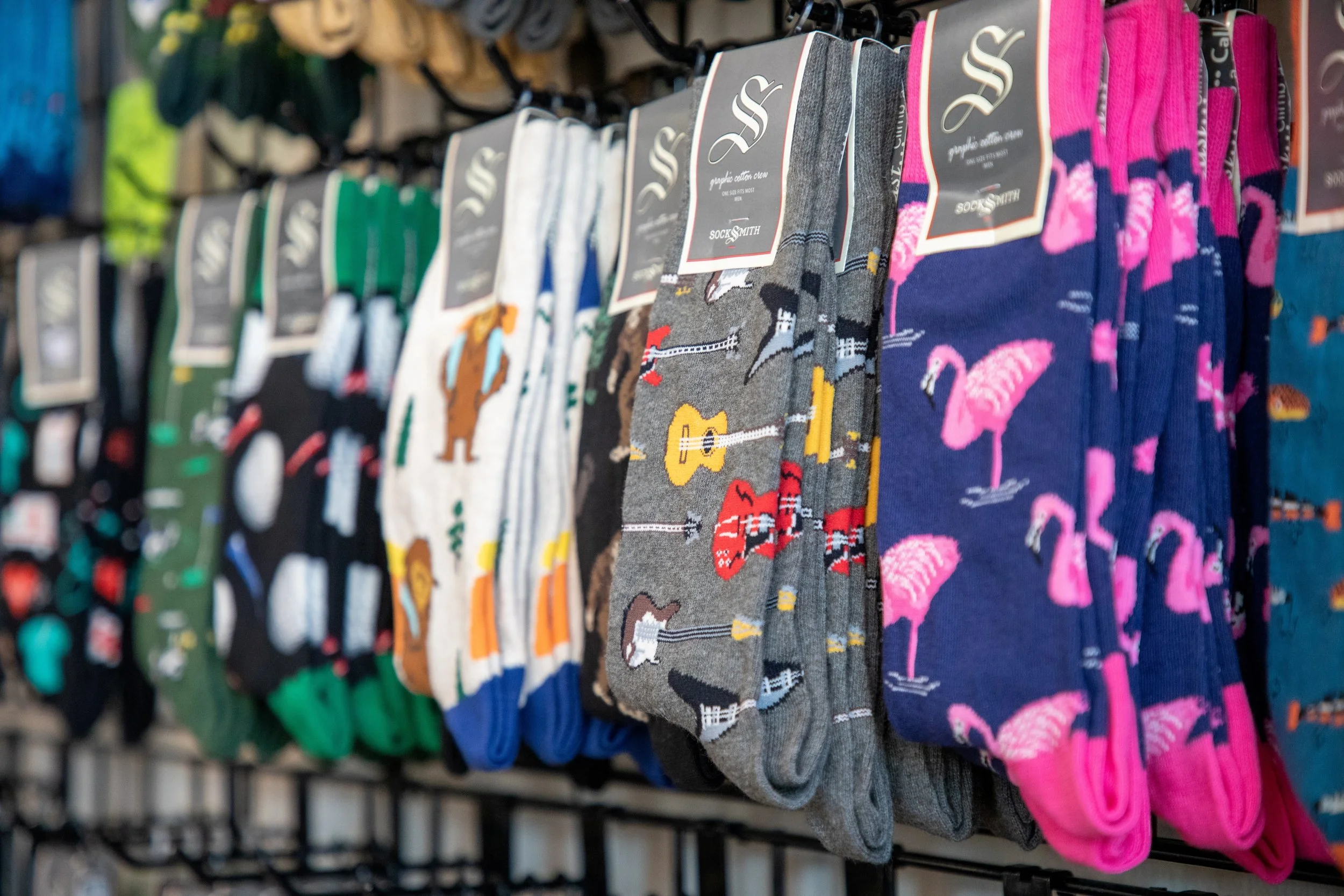 Display of men's socks hanging on a store rack with various colorful and patterned designs.