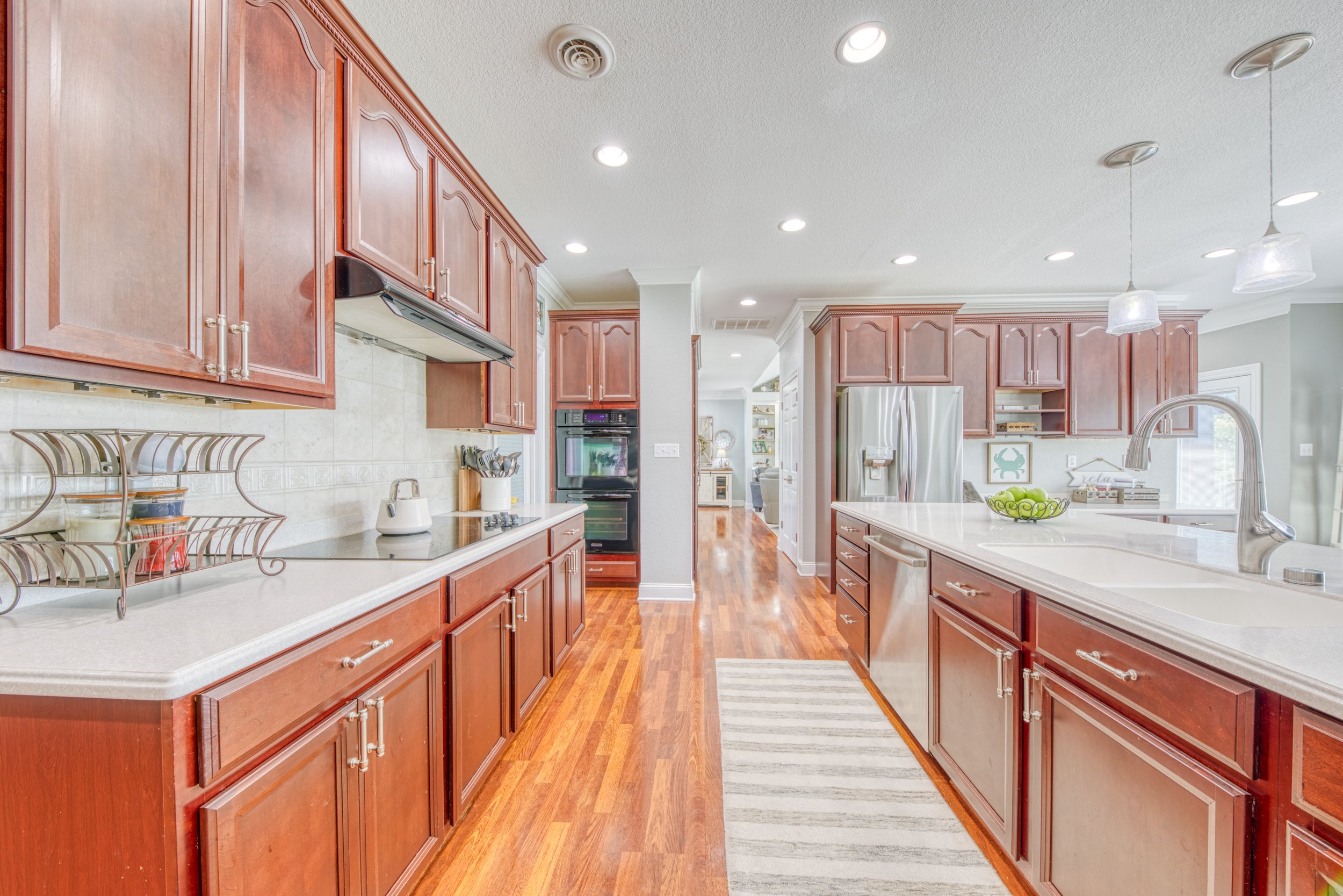 Kitchen with wooden cabinets, white countertops, stainless steel appliances, hardwood floors, and pendant lighting over the kitchen island.