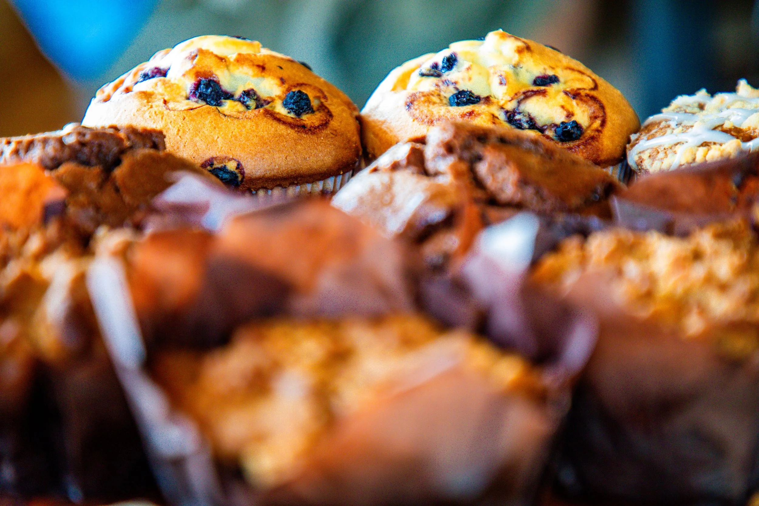 Close-up of blueberry muffins with one muffin in focus, showing blueberries and a golden, baked surface.