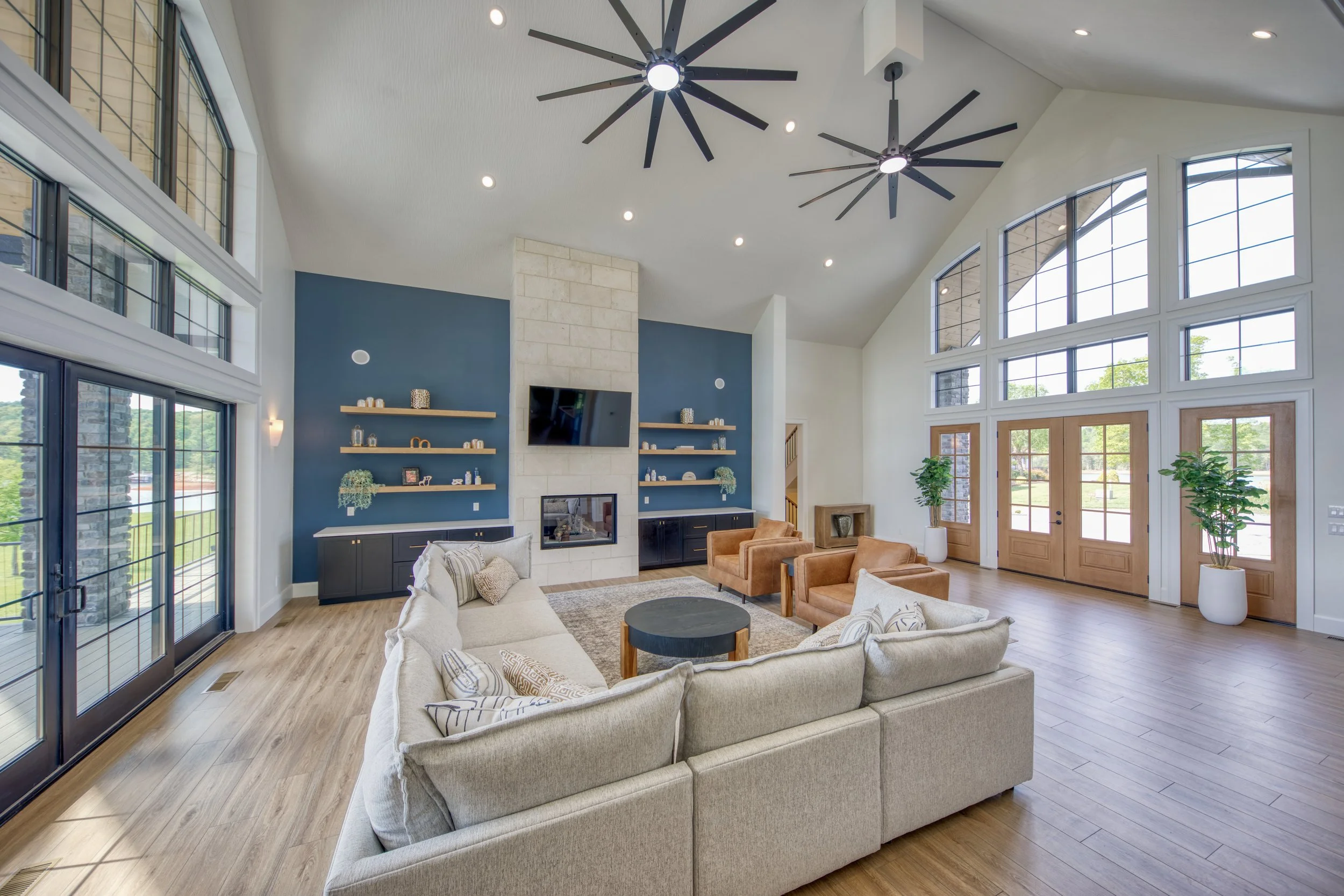 Spacious living room with large windows, high ceilings, modern ceiling fans, a fireplace, built-in shelves, and comfortable seating.