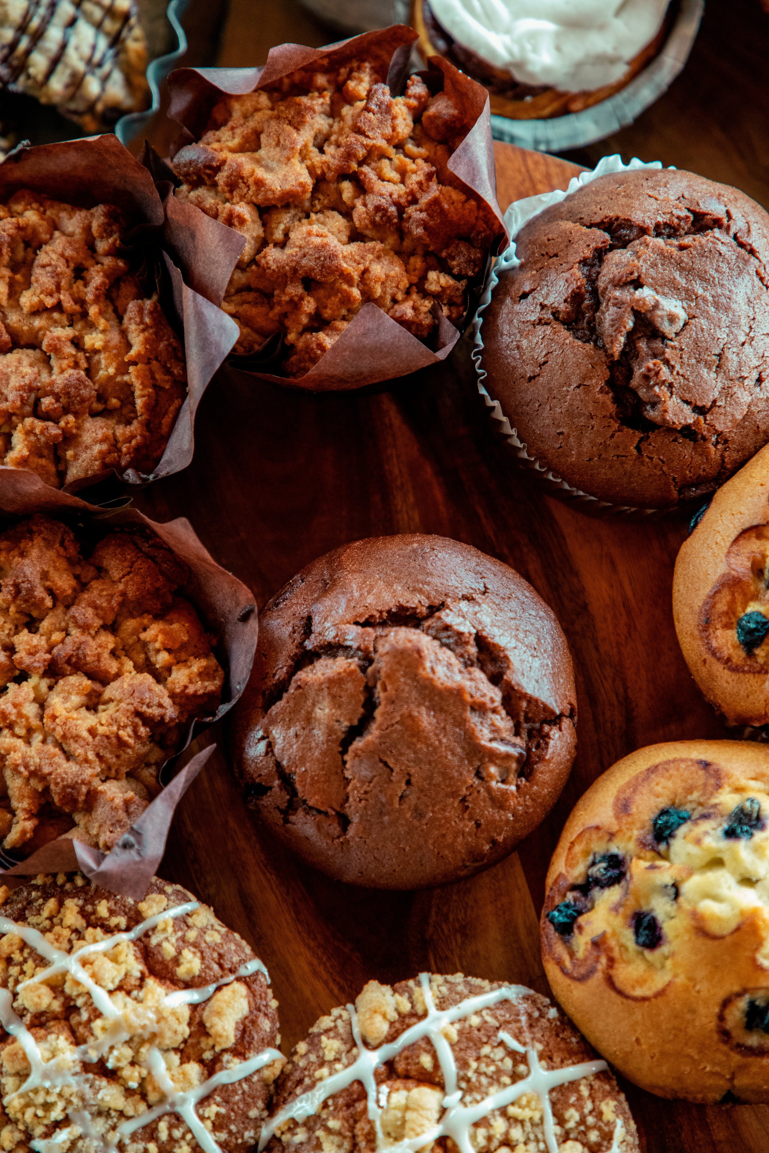 Variety of baked goods including muffins, cookies, and crumb cakes on a wooden surface.