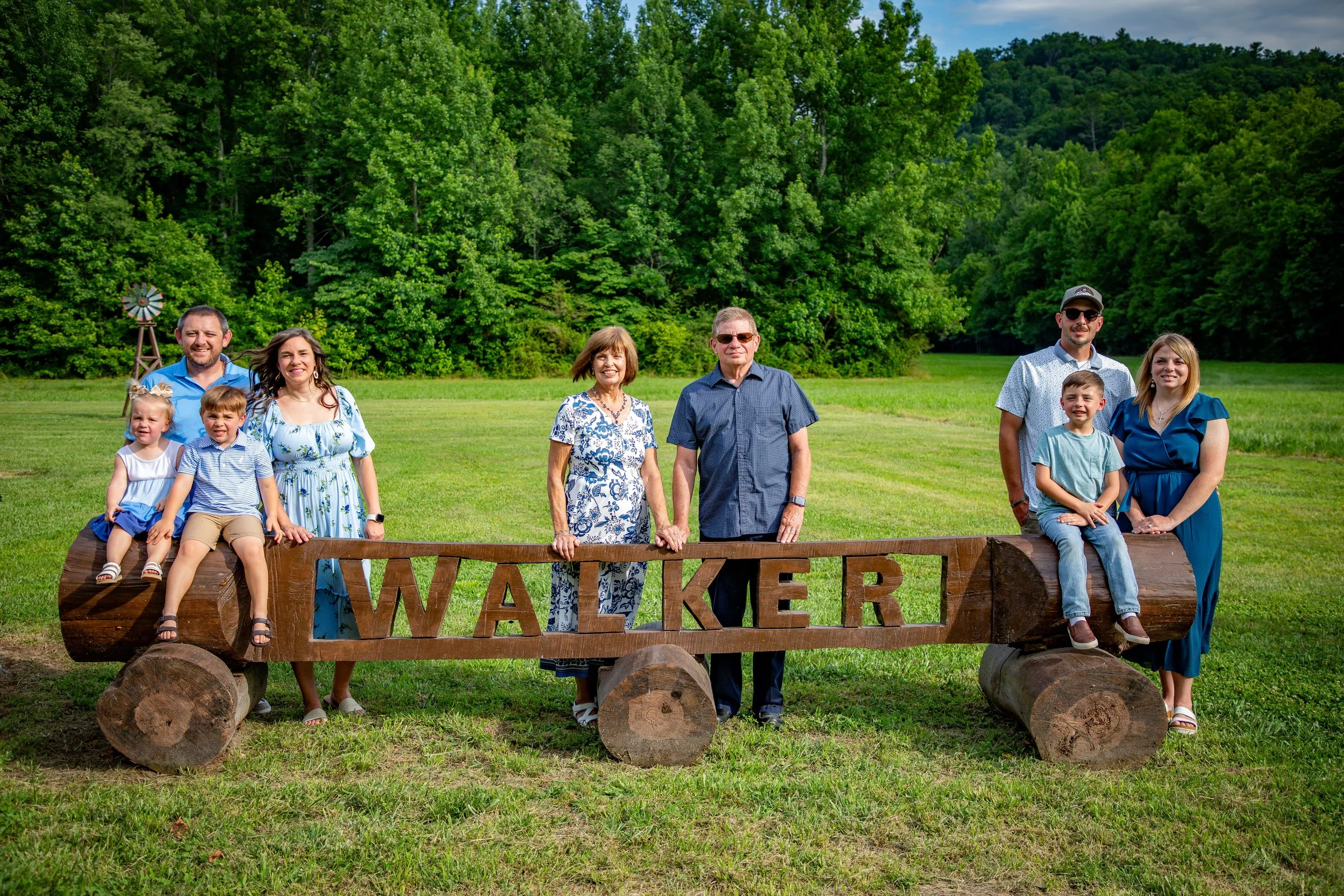 Family group standing by a wooden wagon with a 'WALKER' sign, outdoors on a grassy field with green trees in the background.
