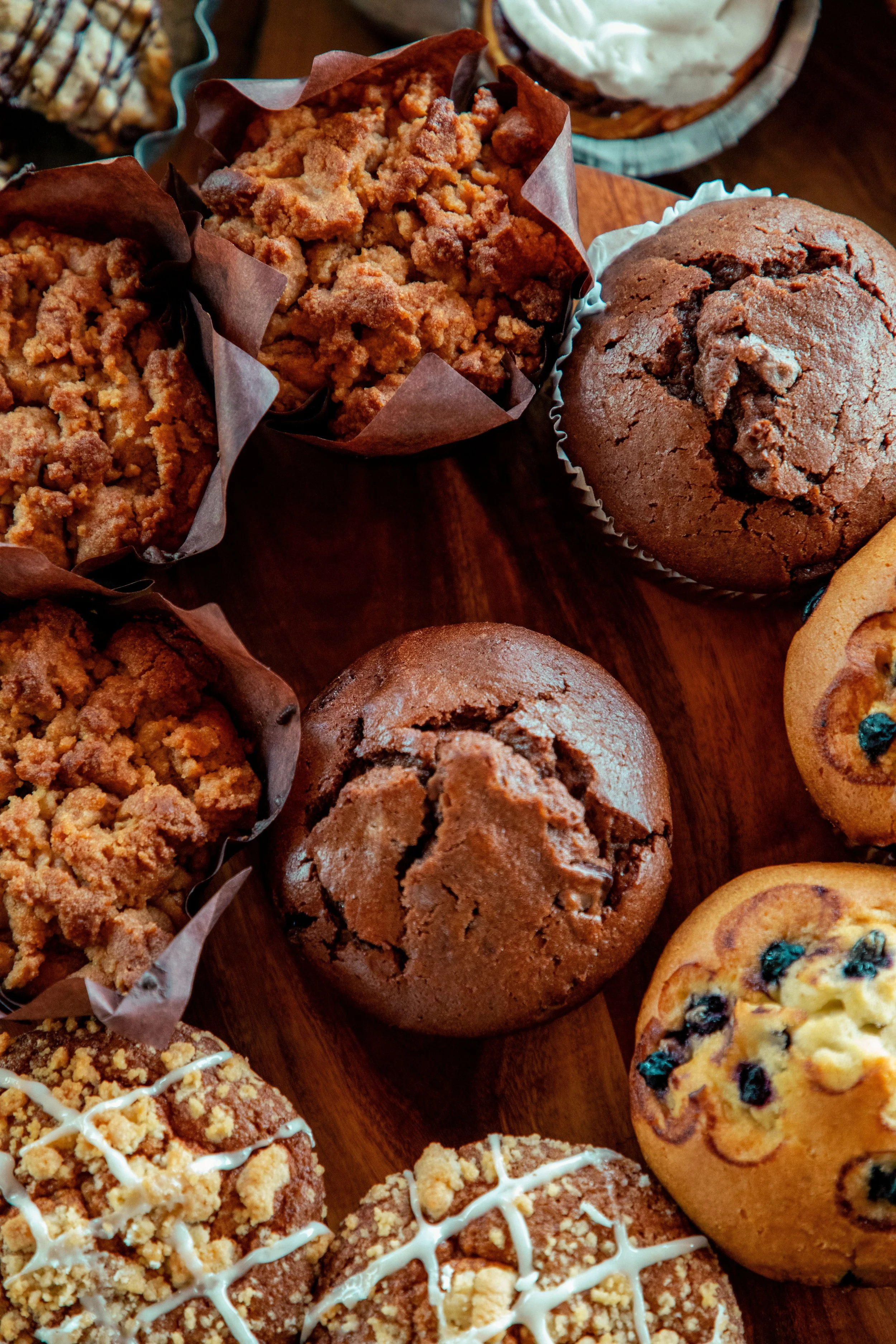 Close-up of various cookies on a wooden surface, including crumbly cookies with powdered sugar, chocolate cookies, and cookies with blueberries.