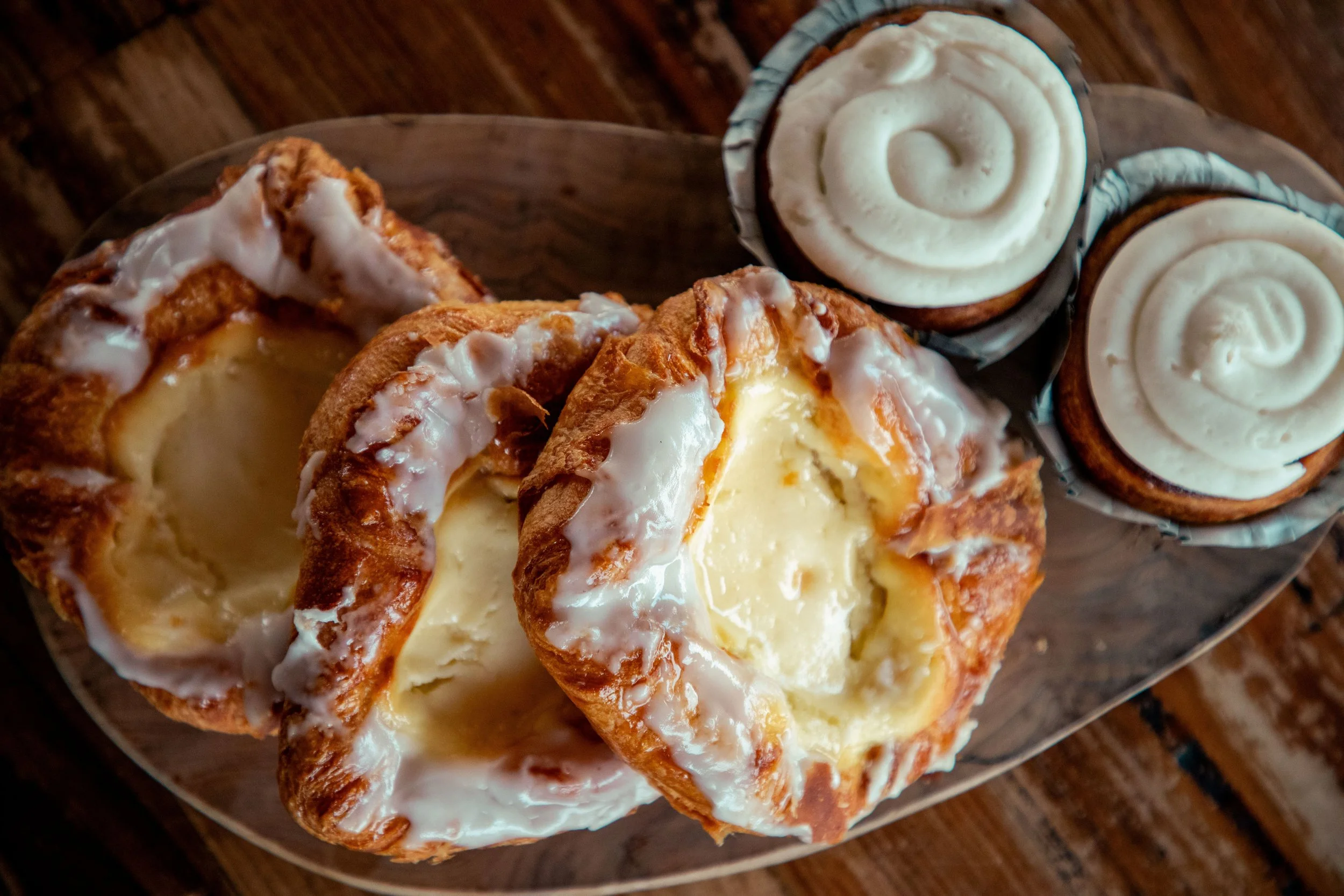 Close-up of a plate with Apple Fritter topped with white icing, and three cupcakes with white swirl frosting on a wooden surface.