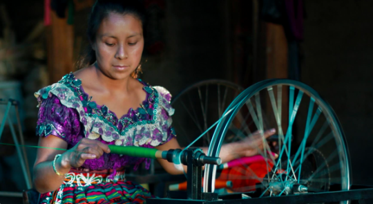 Woman in traditional Guatemalan dress spinning thread on a wheel