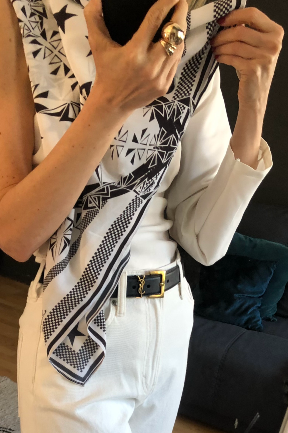 Person in einem weißen Outfit mit schwarzen Akzenten und einer schwarzen Gürtel, die sich vor einem Spiegel fotografiert.