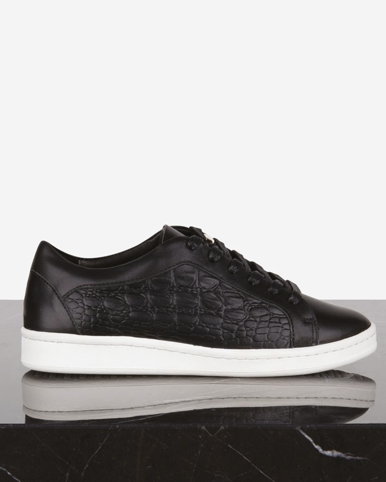 Ein schwarzer Ledersneaker mit Wildleder-Optik und weißer Sohle, auf einem schwarzen und weißen Untergrund