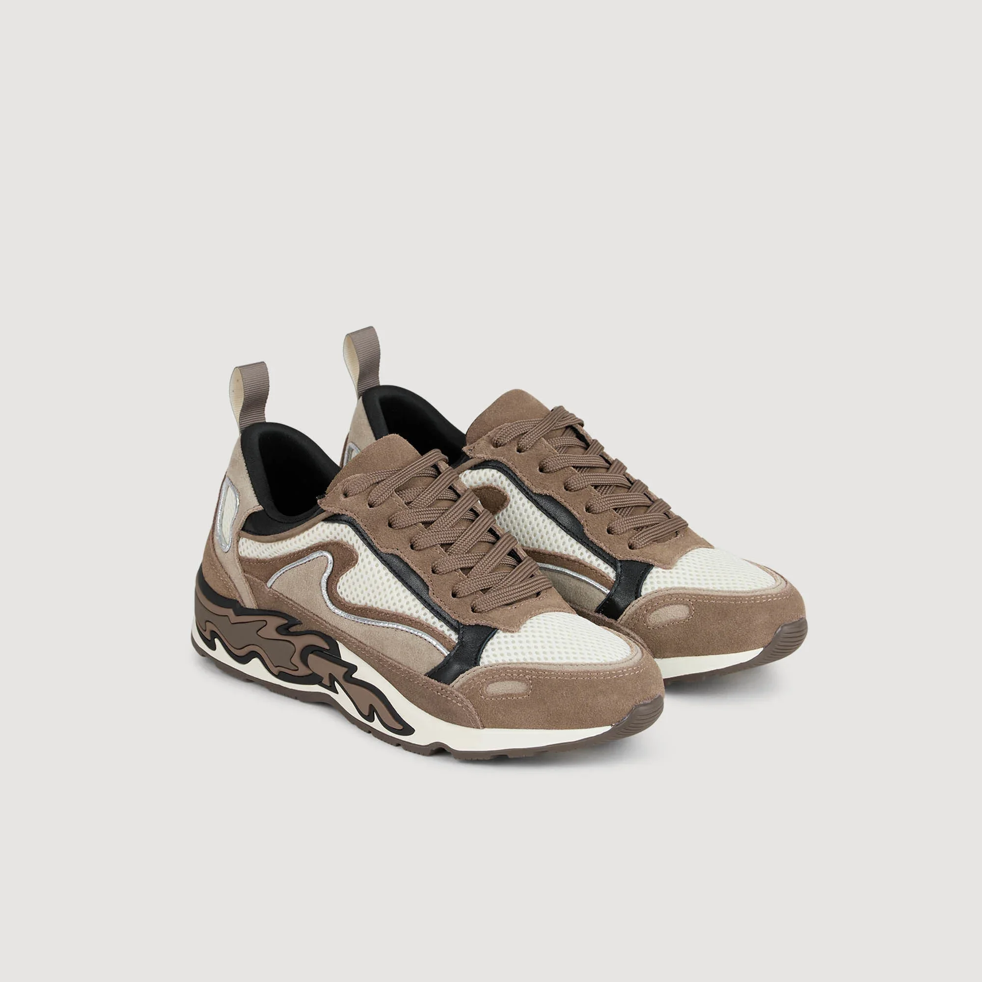 Beige Turnschuhe mit schwarzem Akzent und weißen Mesh-Details auf einer hellgrauen Oberfläche.