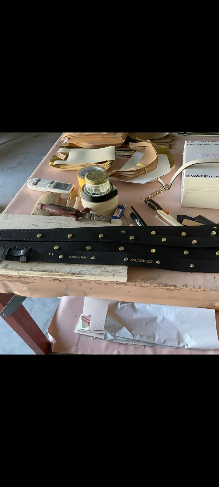 Arbeitsplatz mit Papieren, Schreibwaren, einem Gürtel, Werkzeugen und Organisationselementen auf einem Tisch.