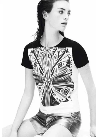 Schwarz-weiß Foto einer jungen Frau mit breiten schwarzen und weißen T-Shirt mit Schmetterlingsmuster, sitzend und in die Ferne blickend.