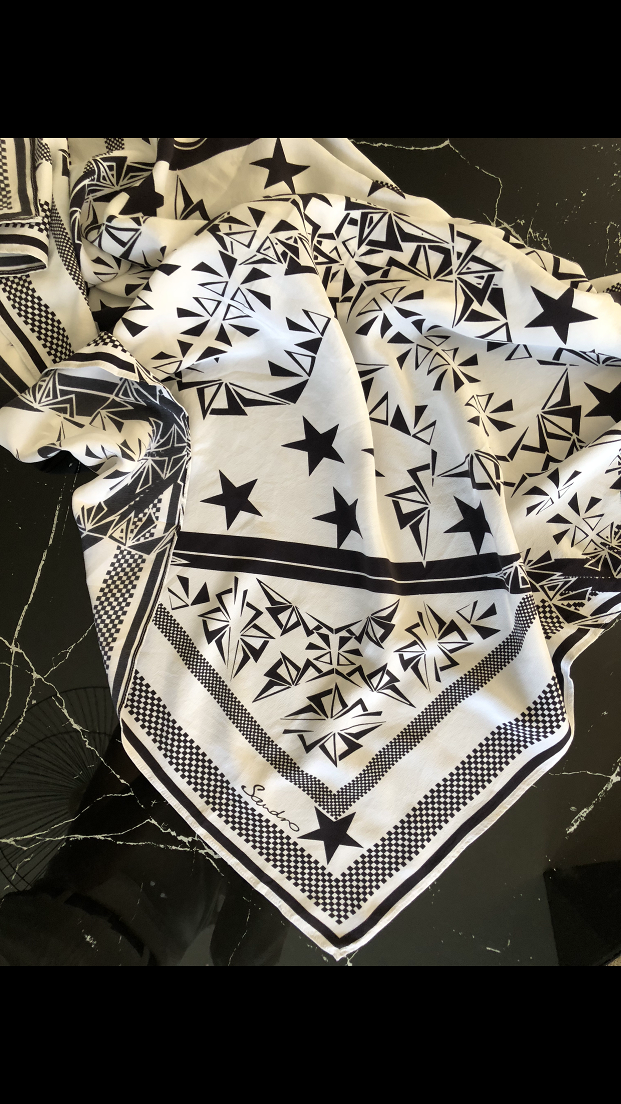 Schwarz-weißer Schal mit geometrischen Designs, Sternen und Mustern, auf schwarzer Marmoroberfläche liegend.