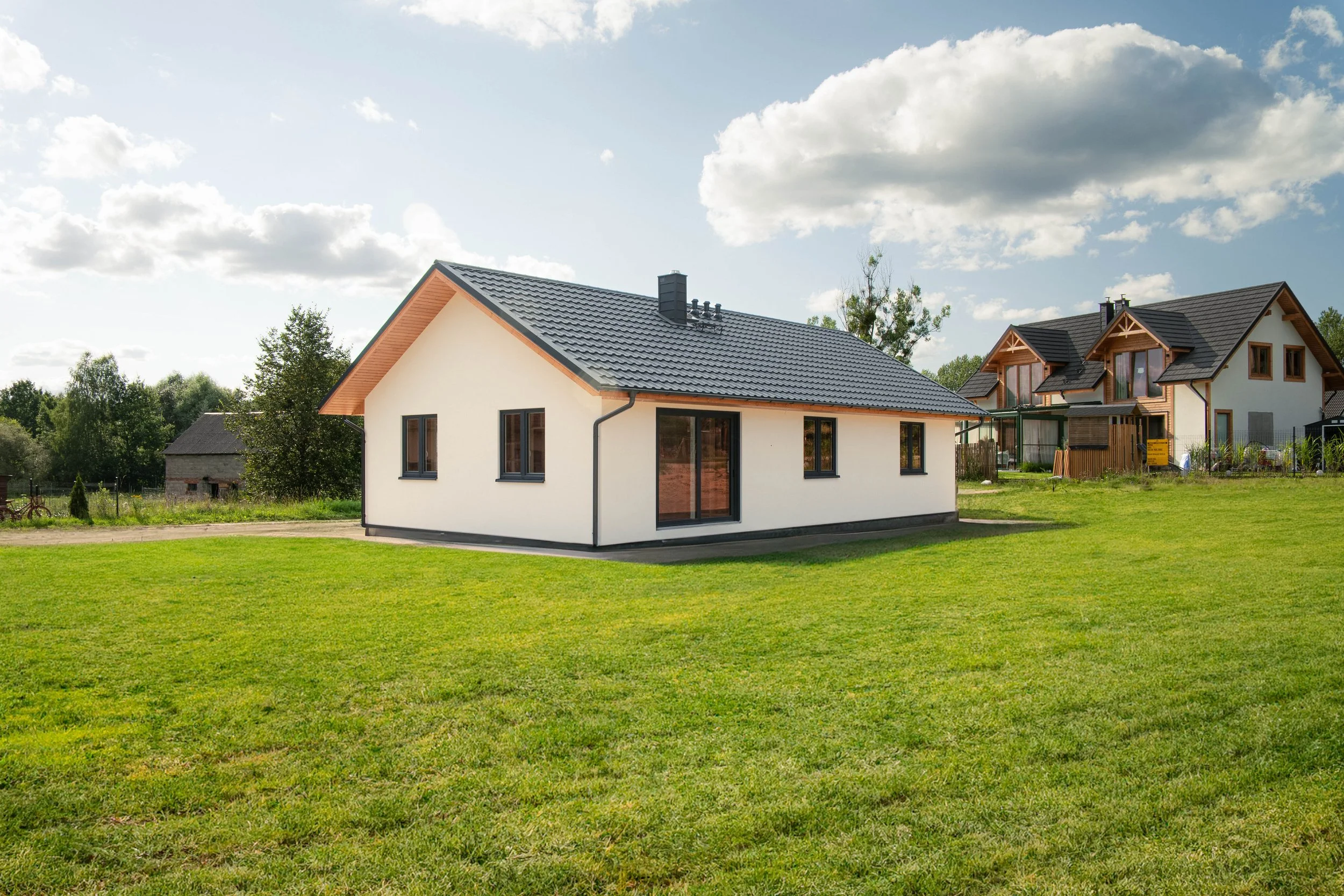 A modern white house with a dark gray tile roof on a grassy yard under a partly cloudy sky.