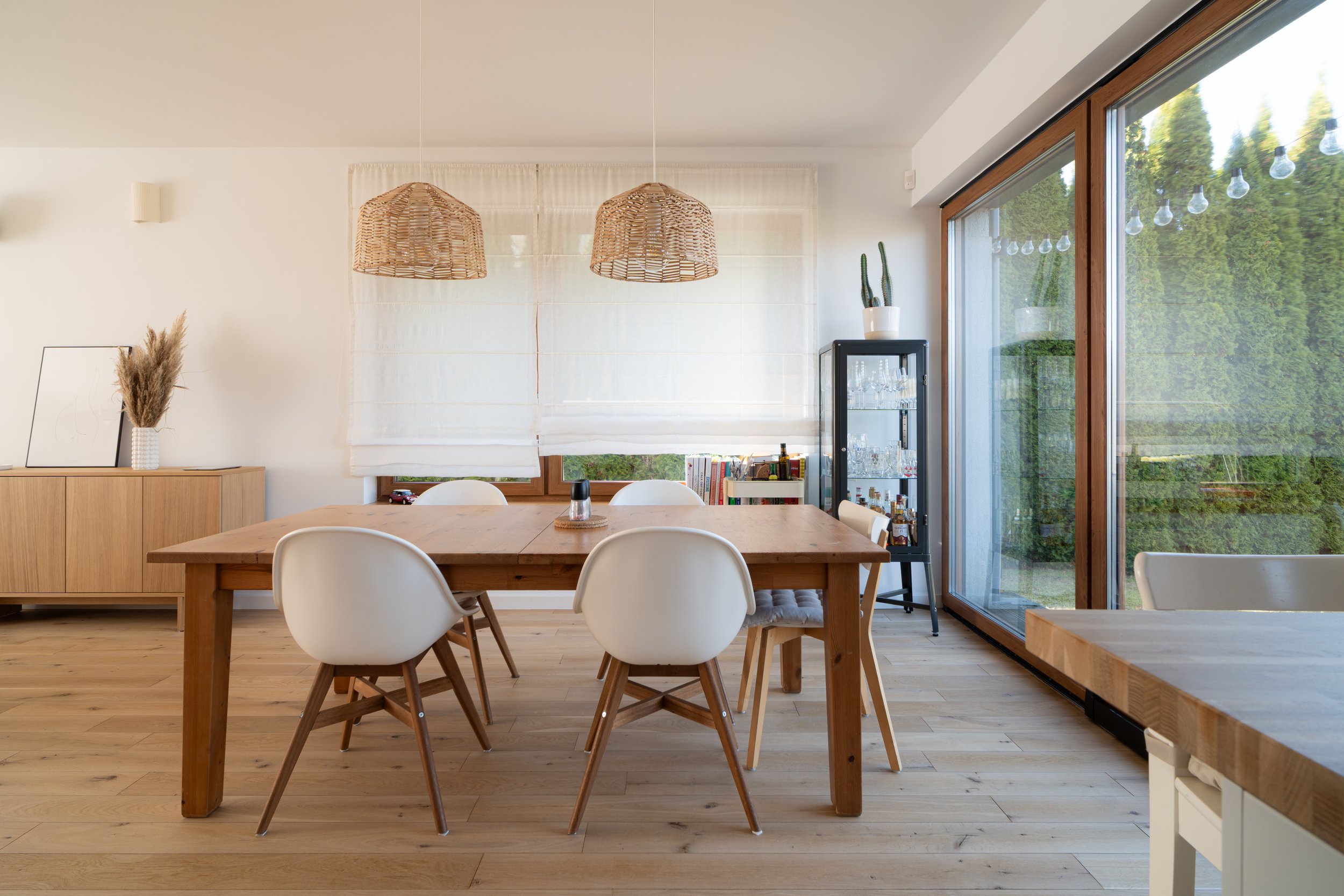 Dining room with wooden table, white chairs, a glass-paned sliding door to a green outdoor view, and wicker pendant lights