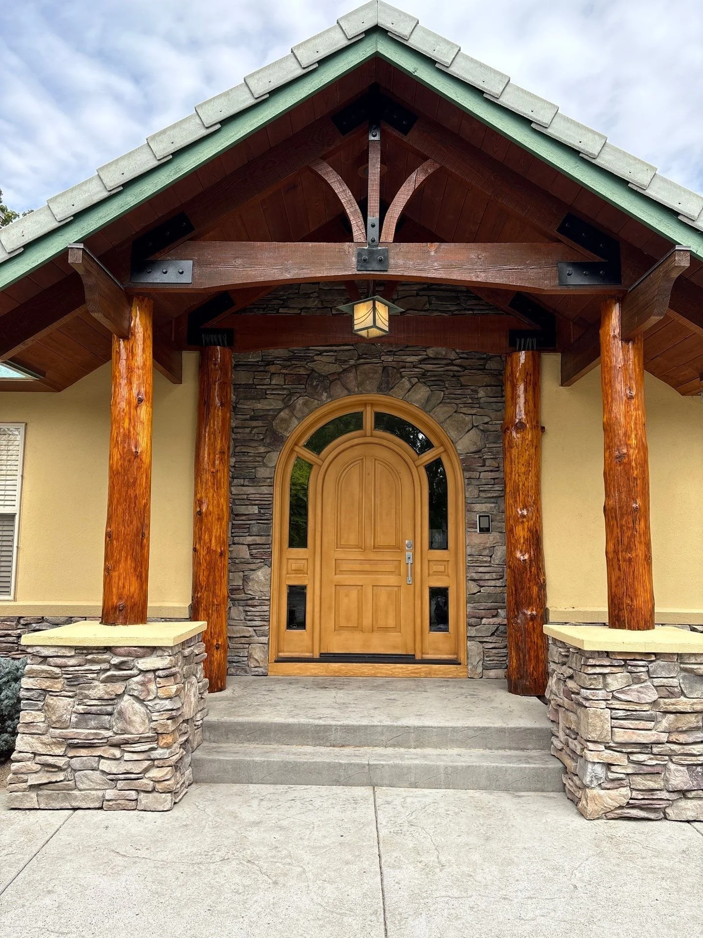 Restained log posts and timber trusses over a stone entry in Sparks