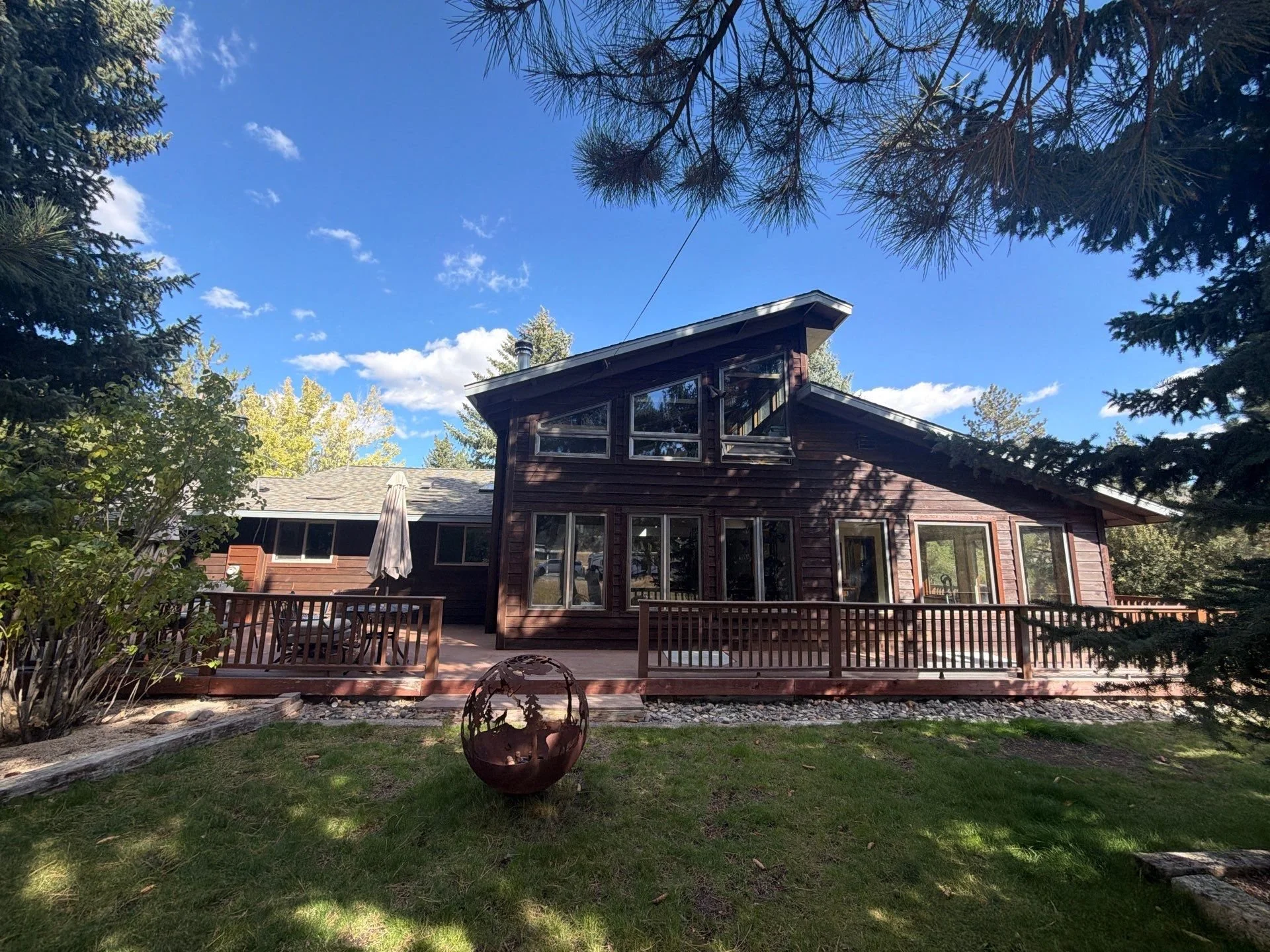 Stained wood-sided home and wraparound deck under tall pines in Verdi